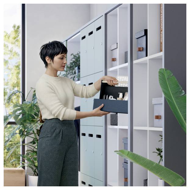 Frau, die Büromaterial in einem Lagerschrank organisiert, zieht eine Schachtel aus einem offenen Regal in einem hellen Büro.