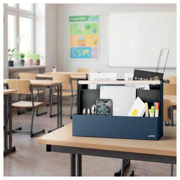 Klassenzimmer in einer Schule mit leeren Schreibtischen und einem Schreibtischorganizer im Vordergrund, der Notizbücher, Stifte, ein Tablet und Schreibwaren enthält.
