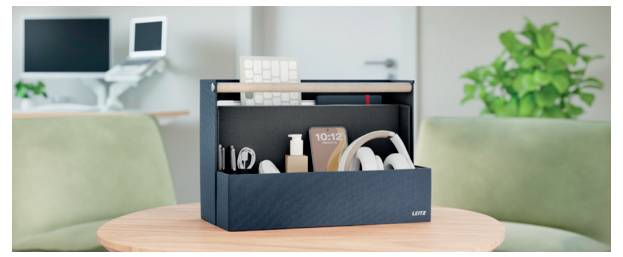 Organisierter Schreibtischorganizer auf einem runden Tisch, der Kopfhörer, Bücher und ein Telefon zwischen zwei Sofas in einem Wohnzimmer hält.