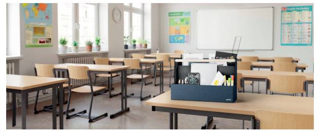 Leeres Klassenzimmer mit Reihen von Schülertischen, einem Lehrertisch, einem Whiteboard, Wandplakaten und Topfpflanzen an den Fenstern.