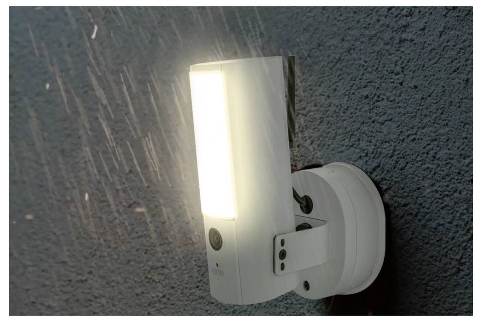 Weiße wandmontierte LED-Außenleuchte, die nachts an einer strukturierten Außenwand leuchtet.