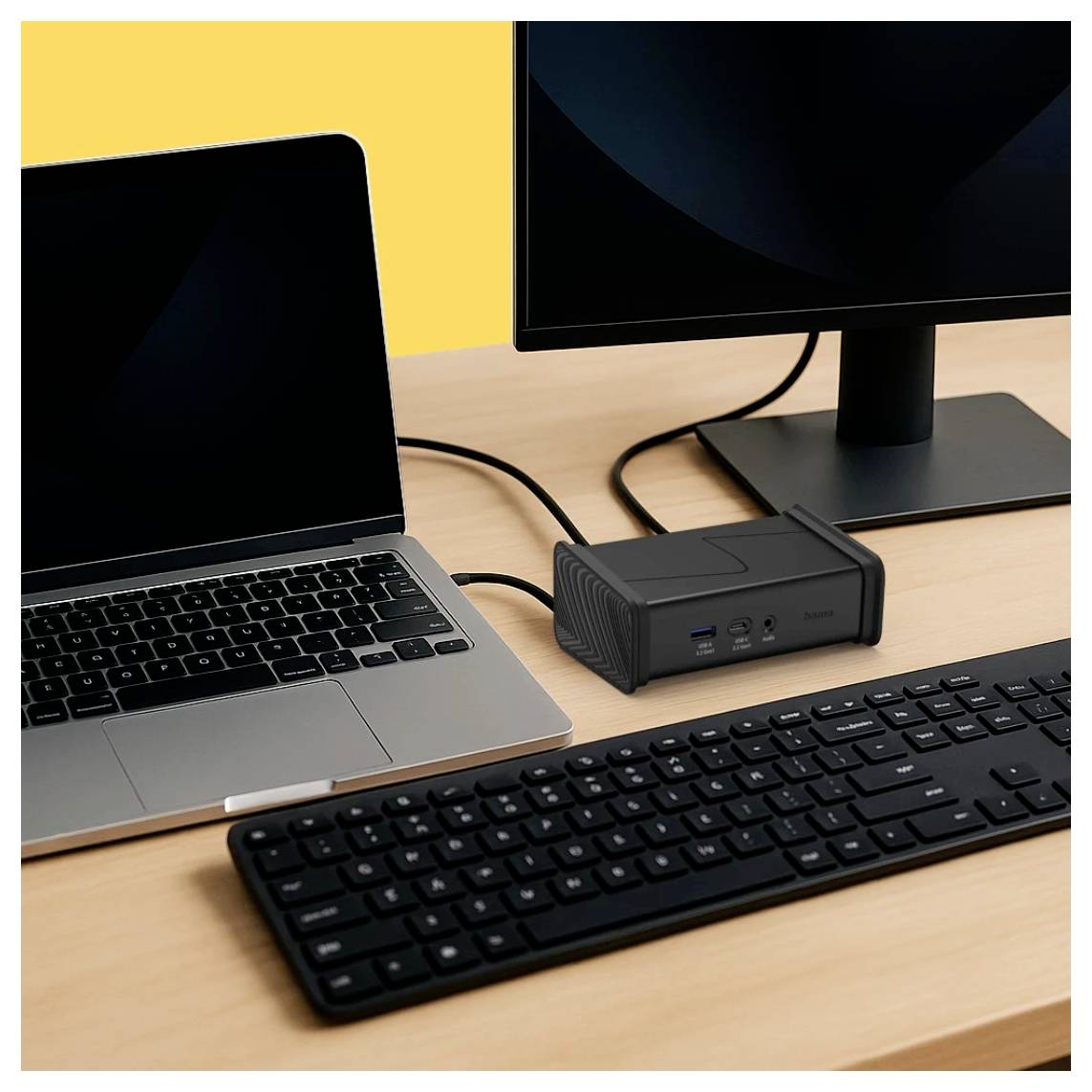 Laptop und externer Monitor auf einem Schreibtisch, verbunden mit einem kleinen Docking-Gerät mit einer Tastatur davor, was auf eine Arbeitsplatz-Einrichtung hindeutet.