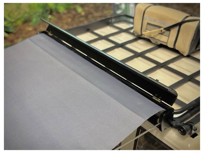 Nahaufnahme einer ausfahrbaren Terrassenmarkise, die über einen Metallrahmen teilweise ausgefahren ist, mit der sichtbaren aufgerollten Stoffabdeckung an einem Ende.