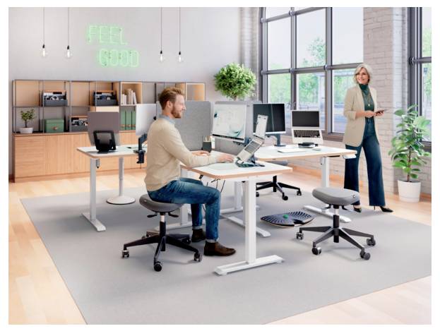 Modernes offenes Büro mit einem Mann, der an einem Schreibtisch arbeitet, und einer Frau, die in der Nähe steht, mit Computern, Regalen, Pflanzen und einem Leuchtreklame-Schild mit der Aufschrift 