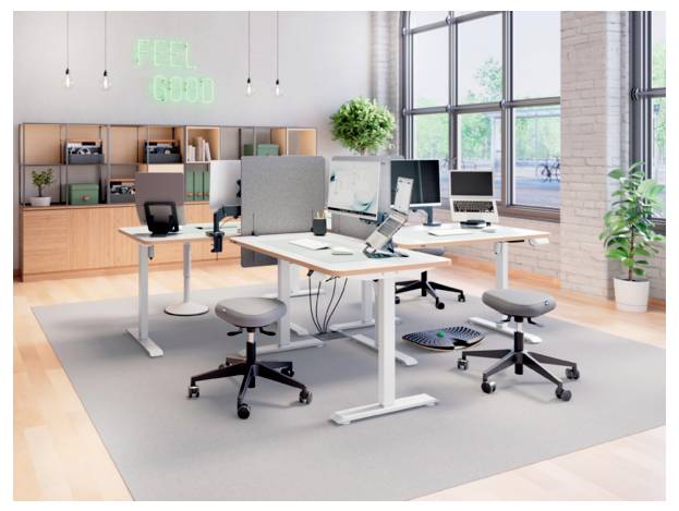 Modernes Open-Space-Büro mit verstellbaren Schreibtischen, Computern, Hockern und einem Neon-Schild mit der Aufschrift „FEEL GOOD