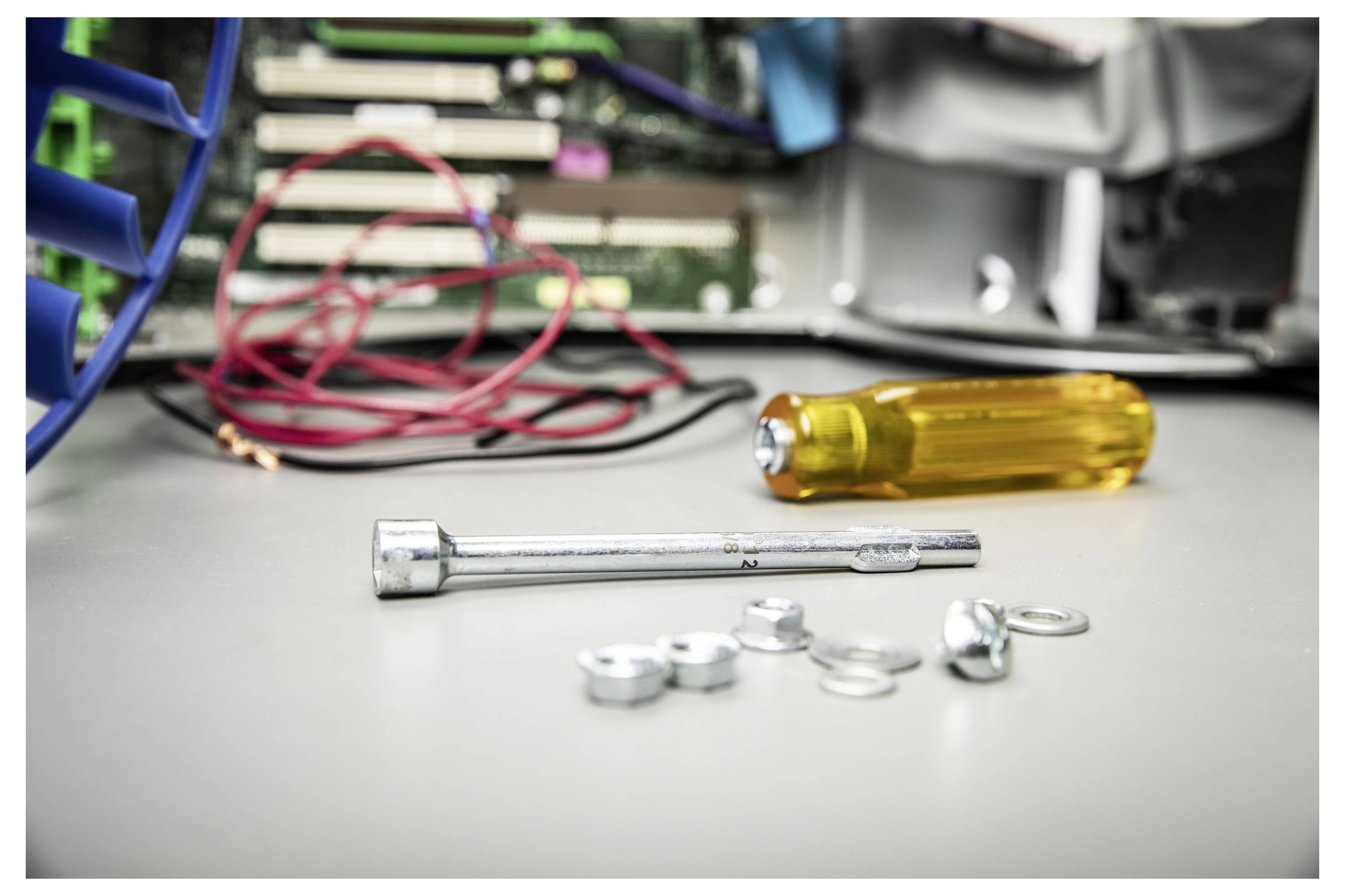 Ein Steckschlüssel, lose Muttern und Unterlegscheiben sowie ein Schraubenzieher auf einer Werkbank, mit verwickelten Drähten und elektronischen Bauteilen im Hintergrund.