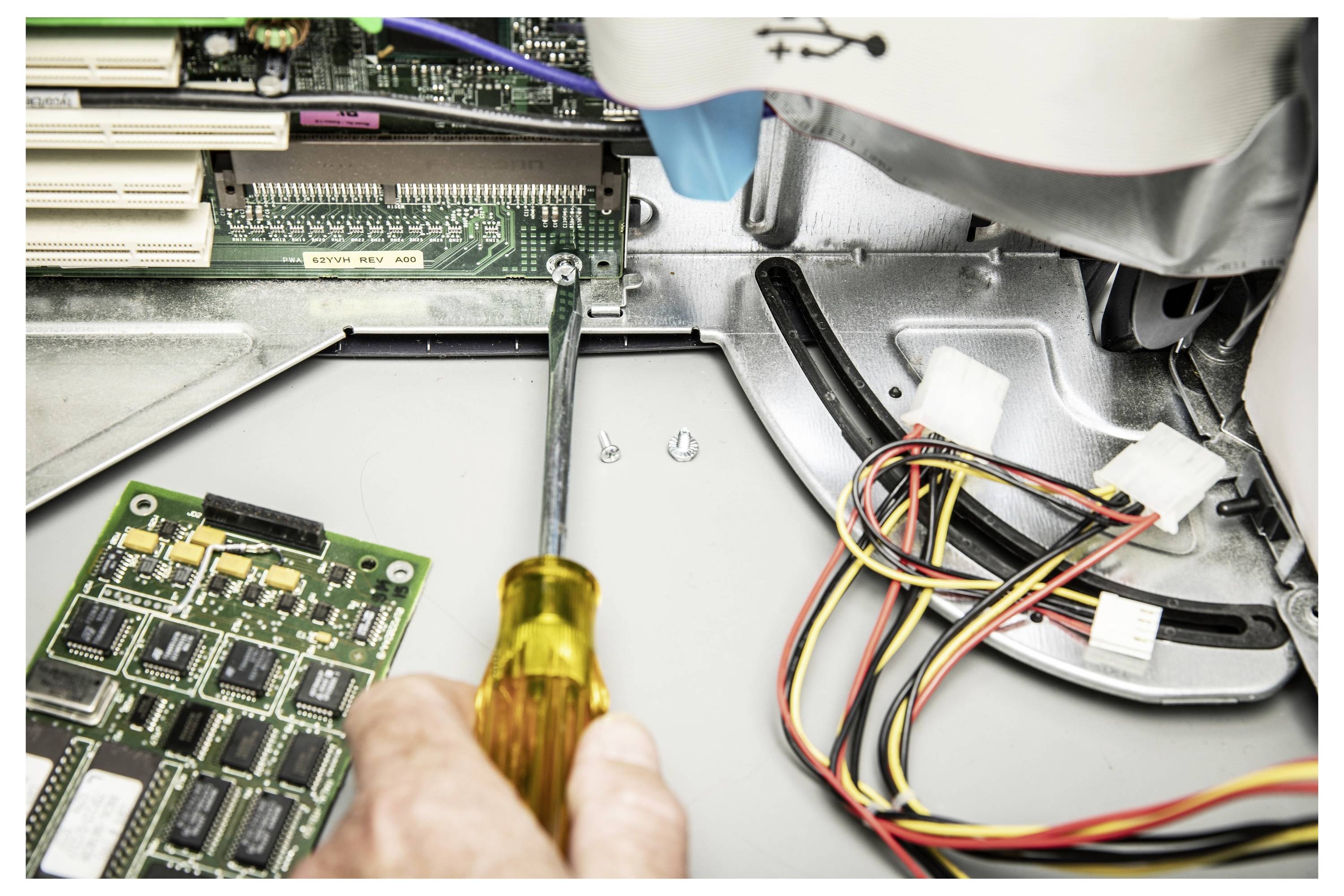 Eine Hand benutzt einen Schraubenzieher, um das Innere eines Computers zu reparieren, wobei Schaltkreise und Stromkabel freigelegt sind.