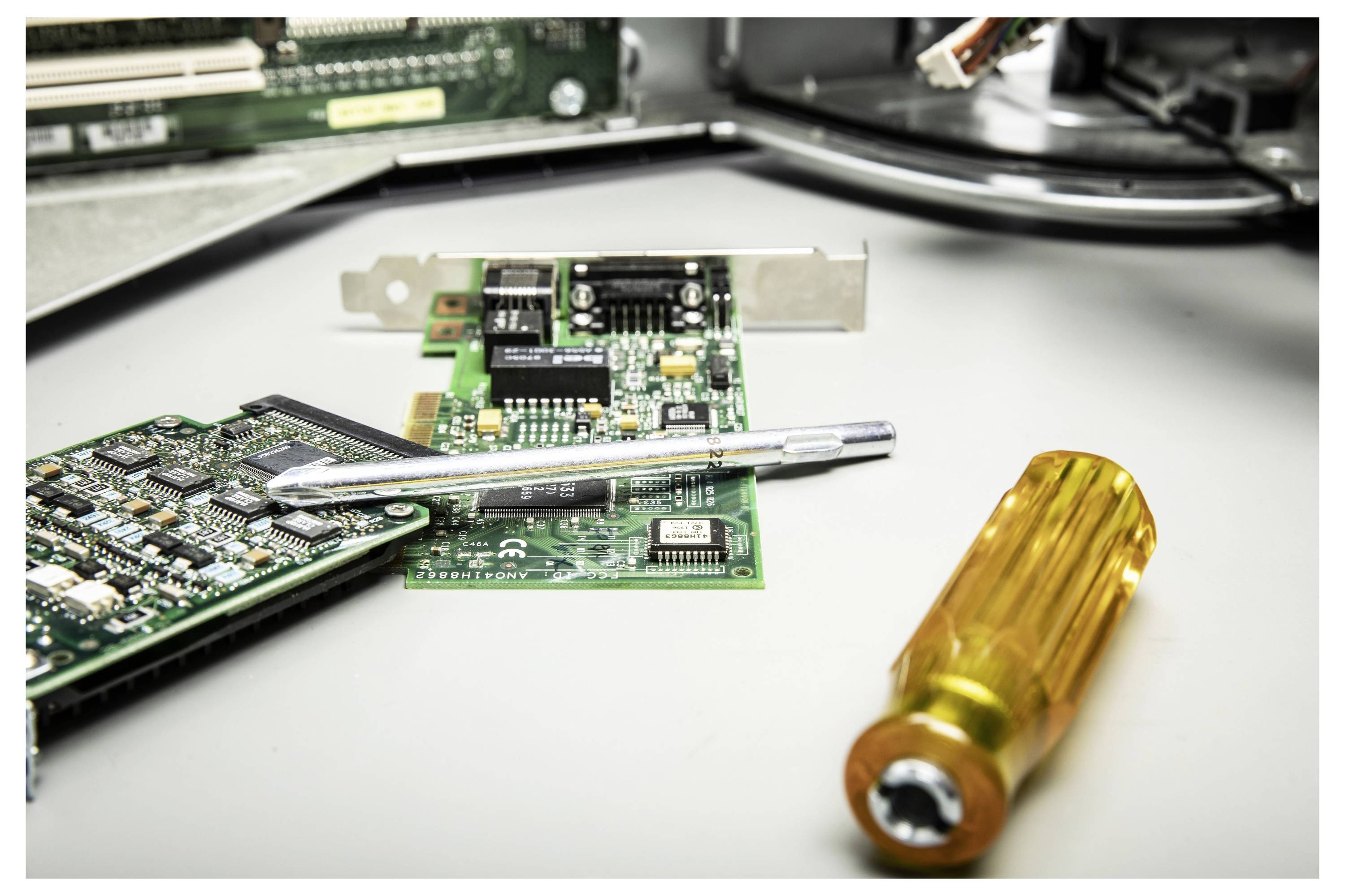 Elektronik-Reparaturszene mit Leiterplatten, einem Schraubendreher und kleinen Komponenten auf einer Werkbank.