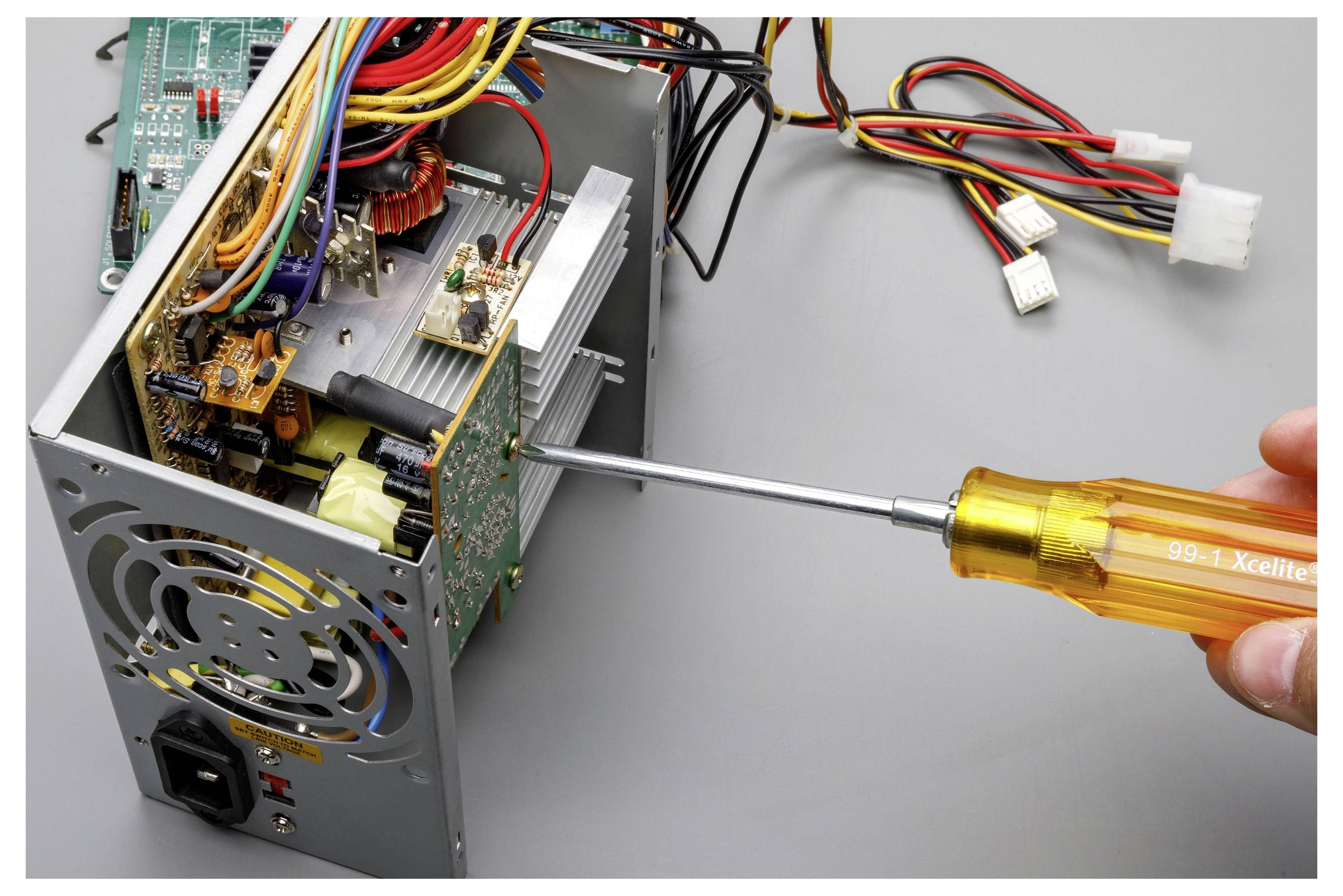 Eine Hand benutzt einen Schraubendreher, um ein Desktop-Computer-Netzteil zu öffnen, wobei interne Komponenten und angeschlossene Drähte freiliegen.