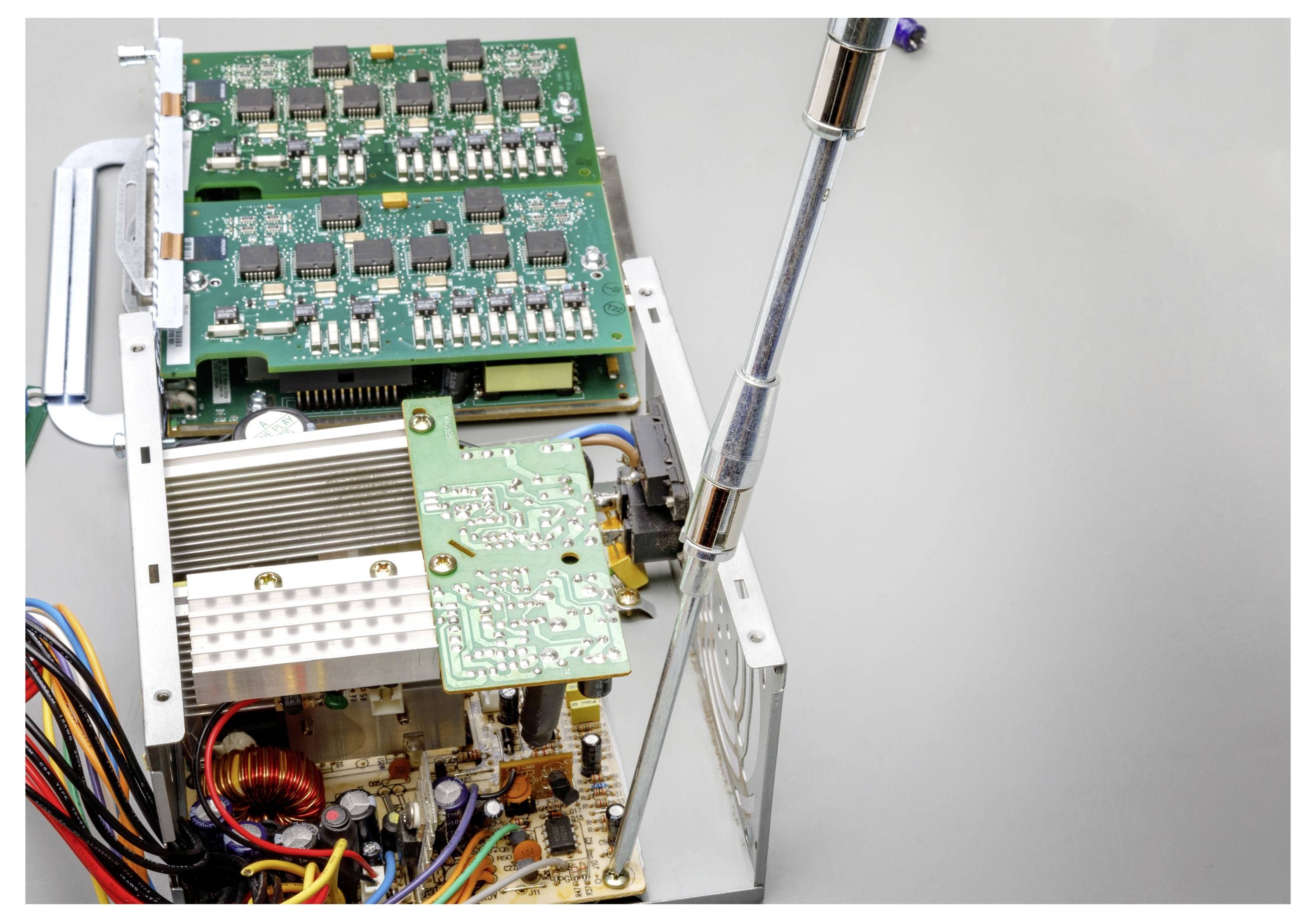 Offenes elektronisches Gerät mit Leiterplatten und Verdrahtung, die mit einem Schraubenzieher justiert werden, zeigt interne Komponenten und einen großen Kühlkörper.
