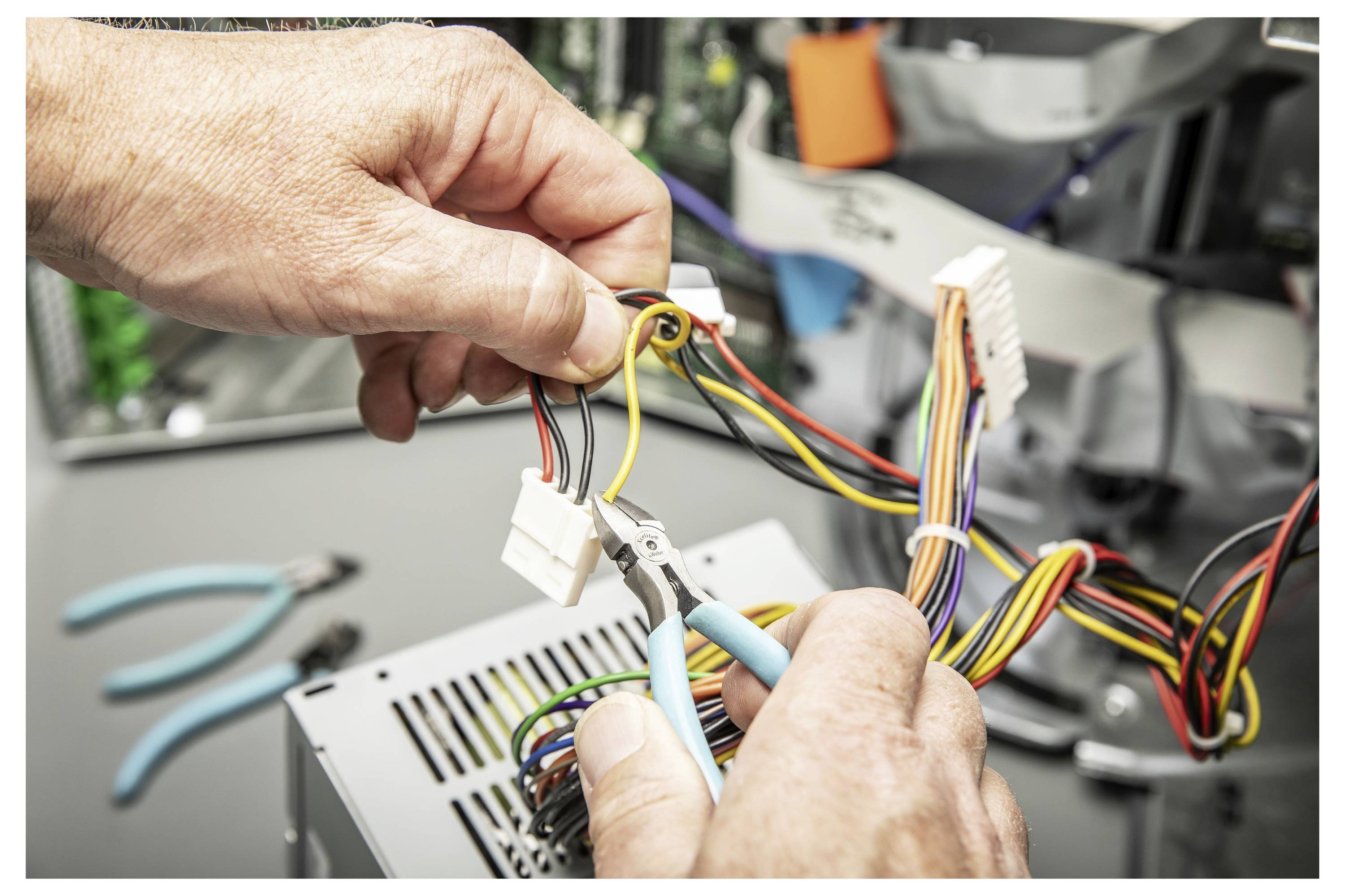 Hände verdrahten einen Computerstromversorgungsstecker mit einer Zange und verbinden mehrfarbige Kabel in elektronischen Geräten.