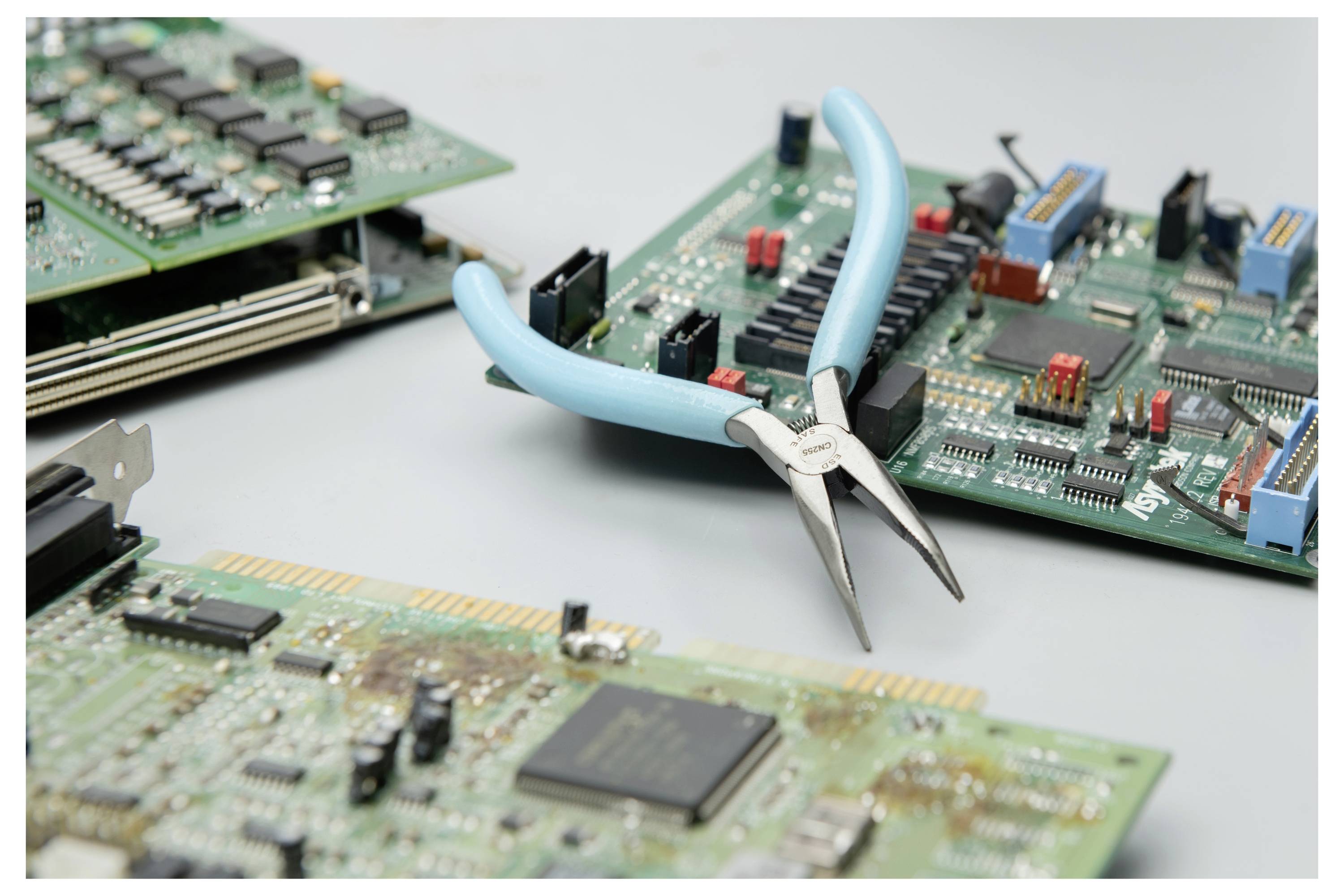 Blaugriffige Zange, die auf zerlegten elektronischen Leiterplatten und Computerkomponenten auf einer Arbeitsfläche ruht.