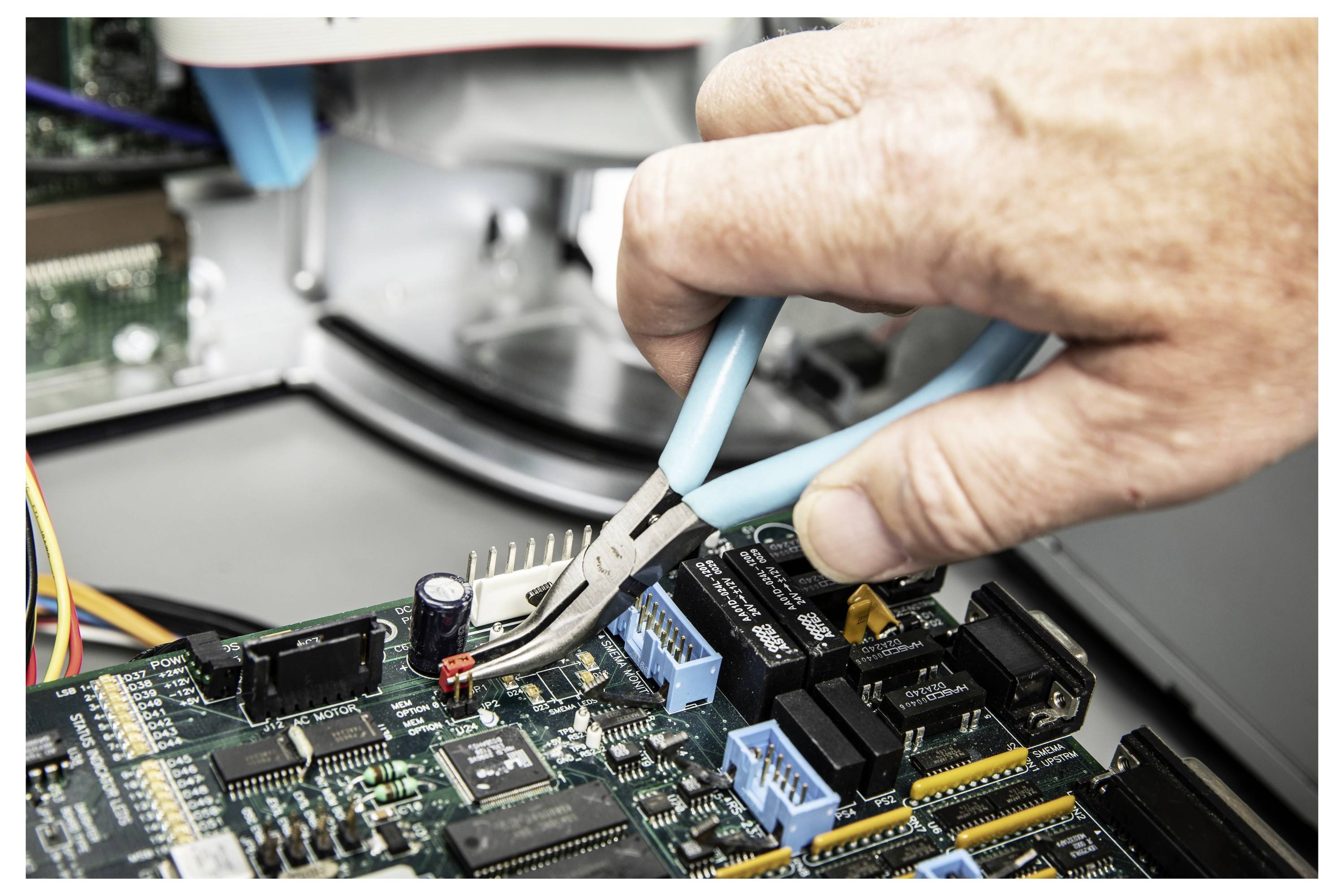 Eine Hand benutzt eine Zange, um eine kleine elektronische Komponente auf einer Leiterplatte während der Reparatur von Computerhardware einzustellen.