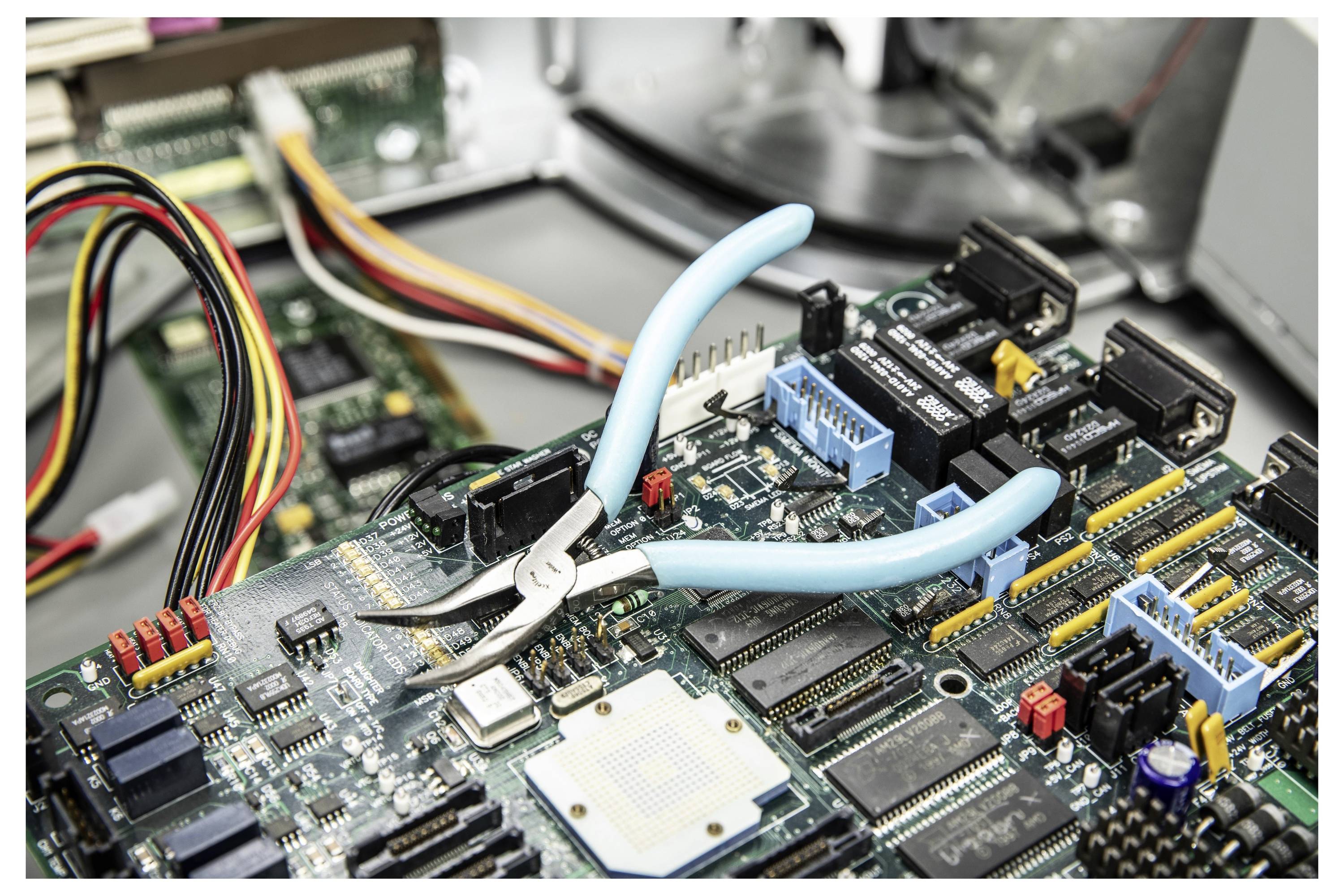 Nahaufnahme einer Zange, die an einer Computerschaltplatine arbeitet, mit verbundenen Drähten und Chips, was auf Elektronikreparatur oder Montage hindeutet.