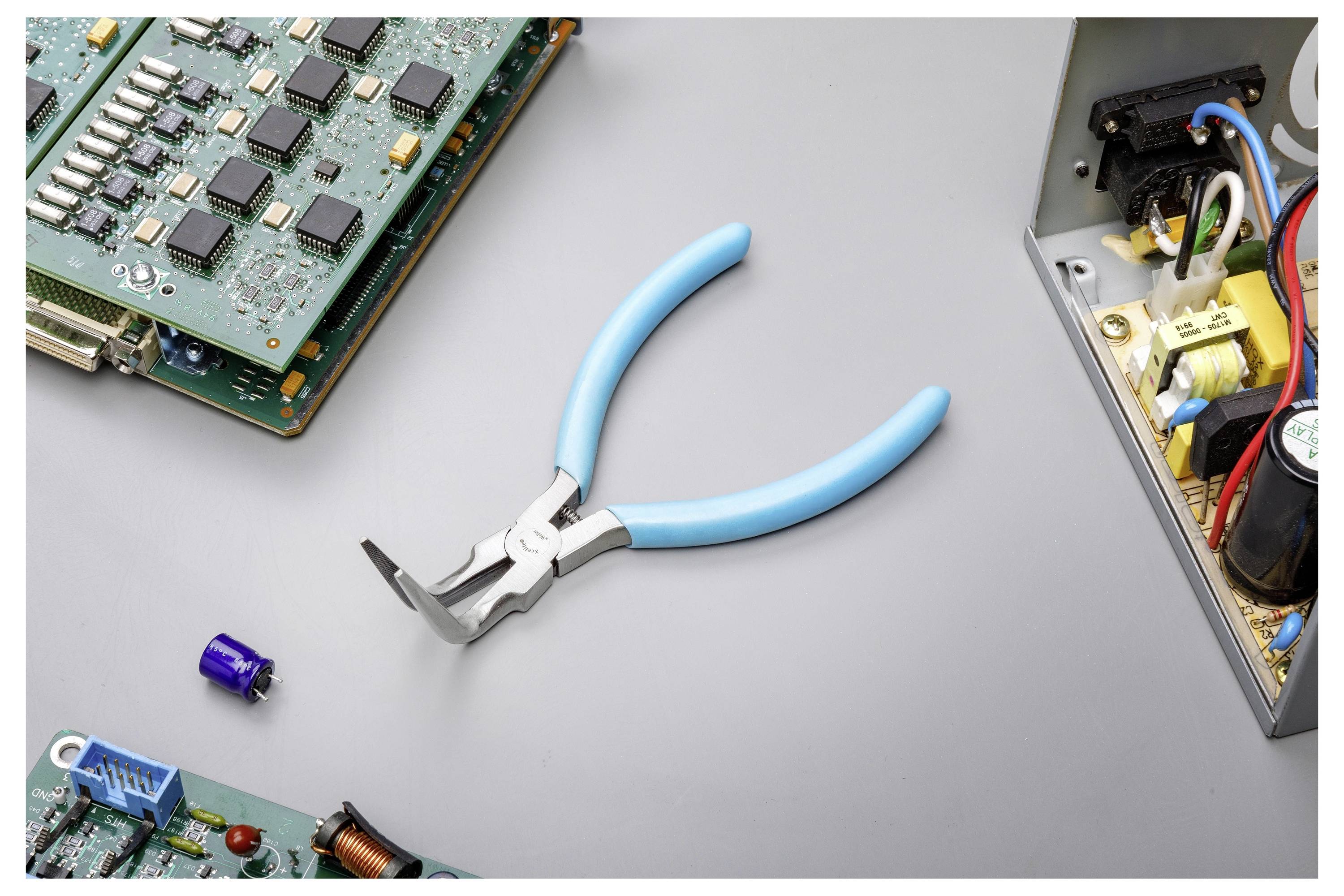 Blaugriffige Drahtschneider auf einer grauen Arbeitsfläche neben freiliegenden Computerplatinen und elektronischen Komponenten, was auf Elektronik-Reparatur oder -Montage hindeutet.