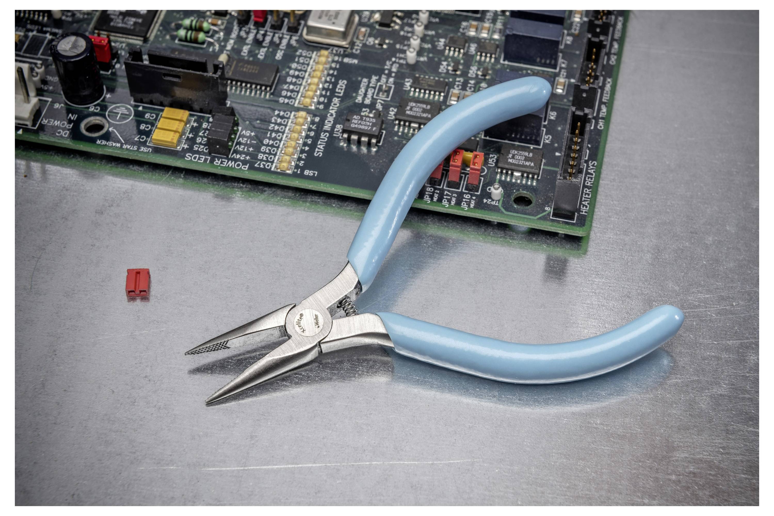 Blaugriffige Spitzenzange ruht auf einer Werkbank neben einer Computerplatine mit einer kleinen roten Komponente in der Nähe.