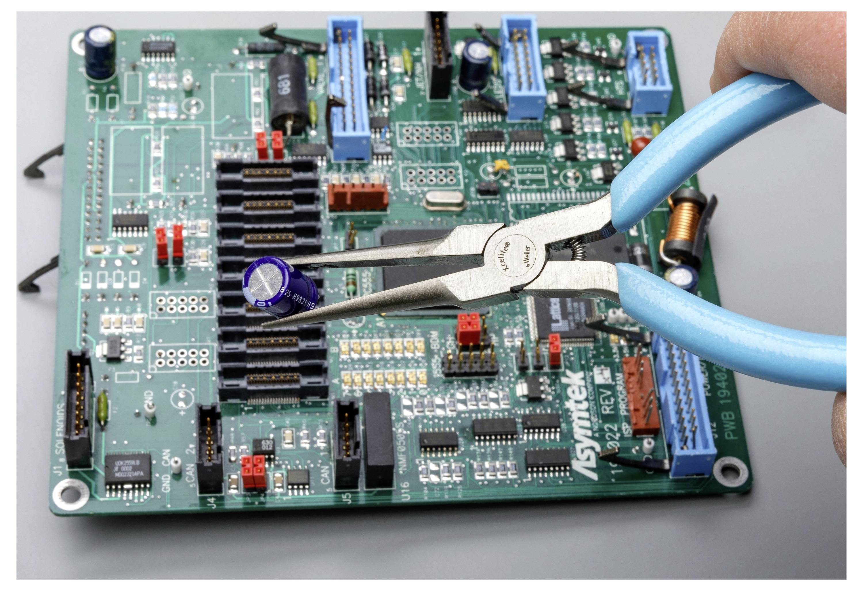 Nahaufnahme einer Zange mit blauem Griff, die eine grüne Leiterplatte mit elektronischen Bauteilen und Steckverbindern hält.