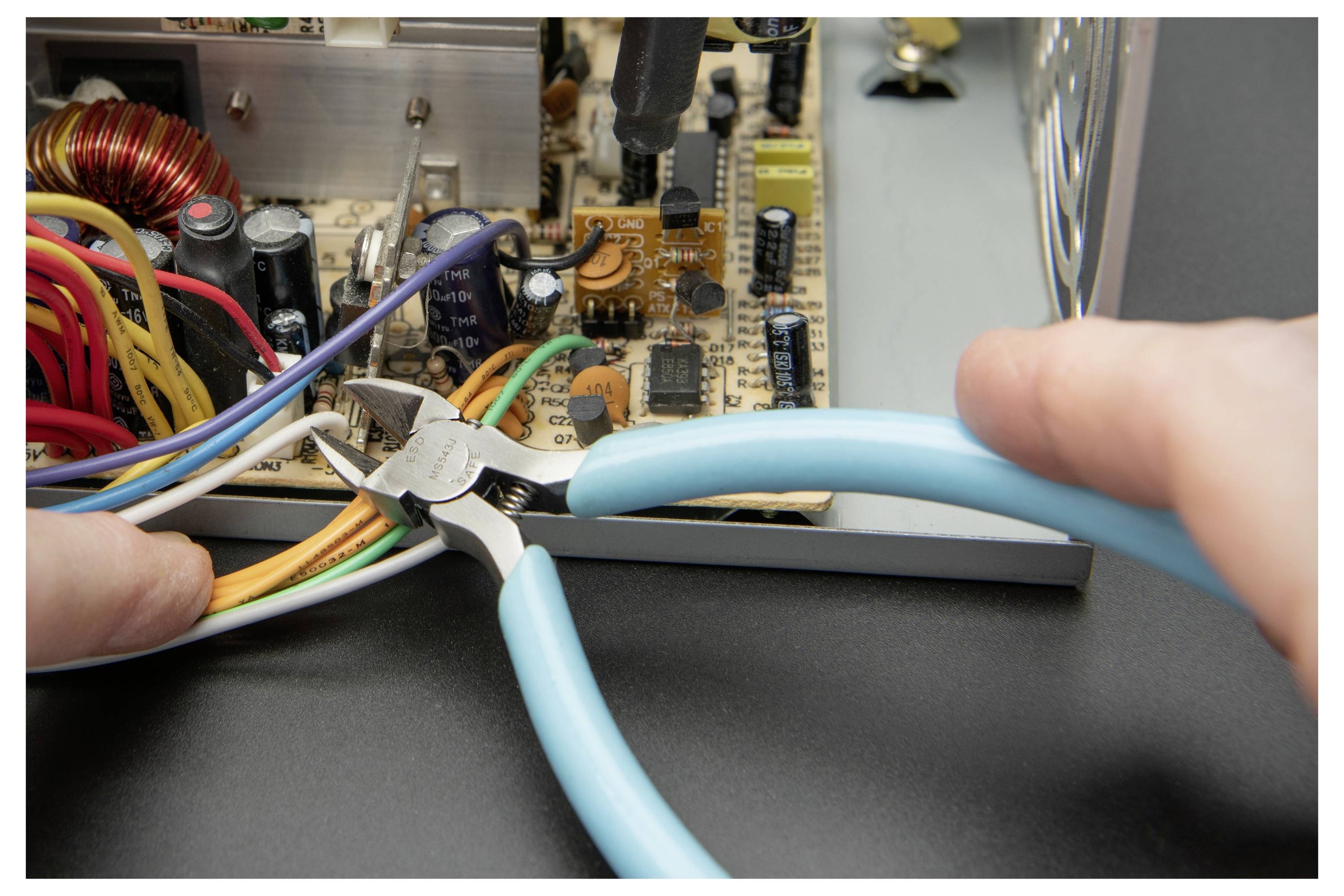 Hände verwenden blaugriffige Zangen zum Schneiden von Drähten in einem offenen elektronischen Stromversorgungsgerät.