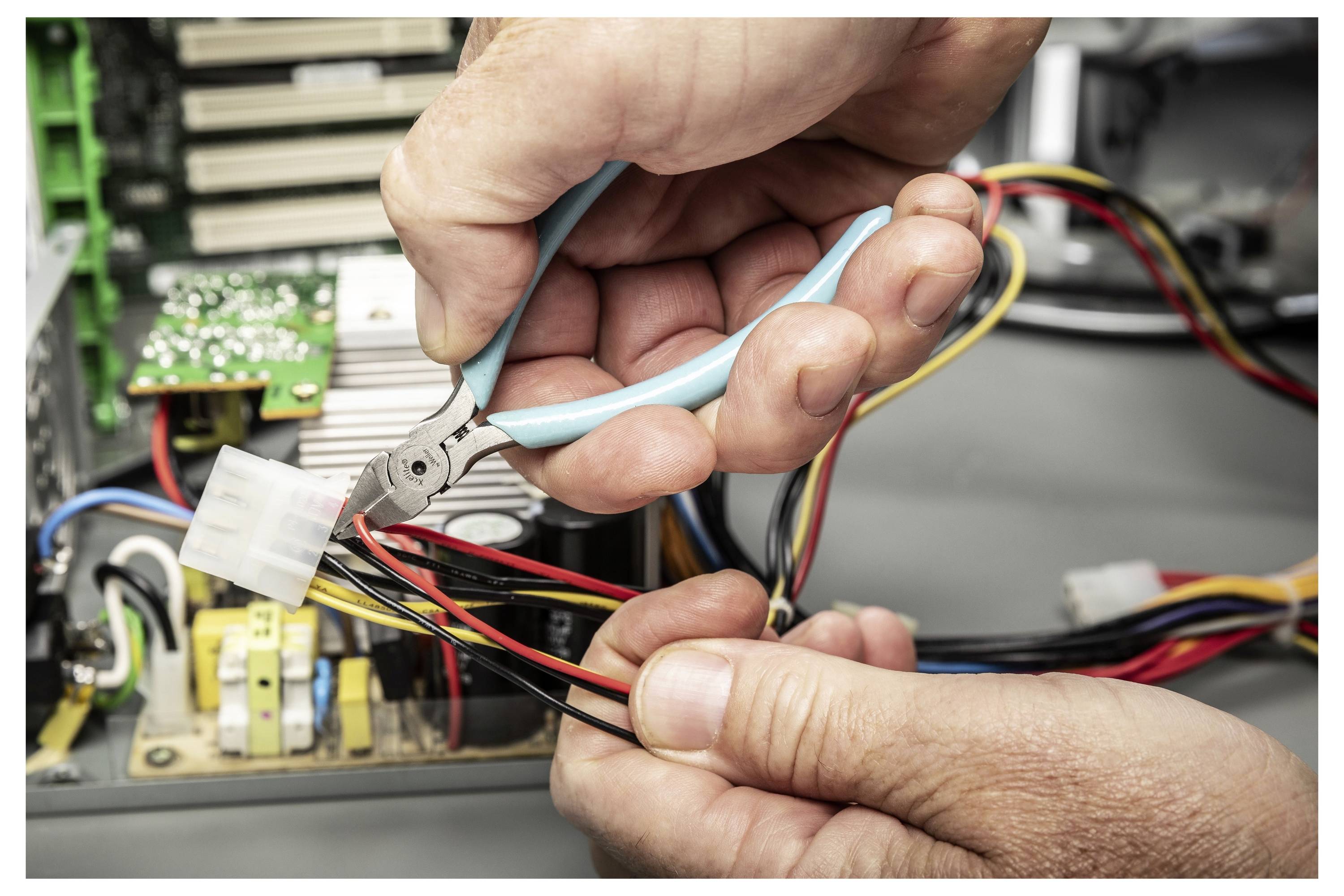 Hände verwenden Zangen zum Schneiden oder Abisolieren von Drähten in einem offenen elektronischen Gerät während einer Reparatur.