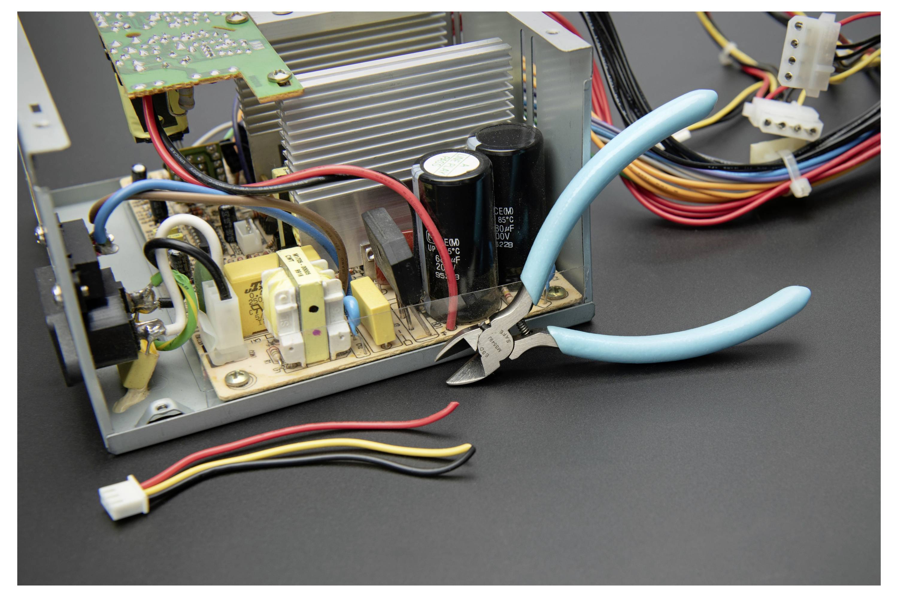 Nahaufnahme eines offenen elektronischen Geräts mit interner Verkabelung und einer Leiterplatte, mit blaugriffigen Zangen neben den freiliegenden Komponenten.