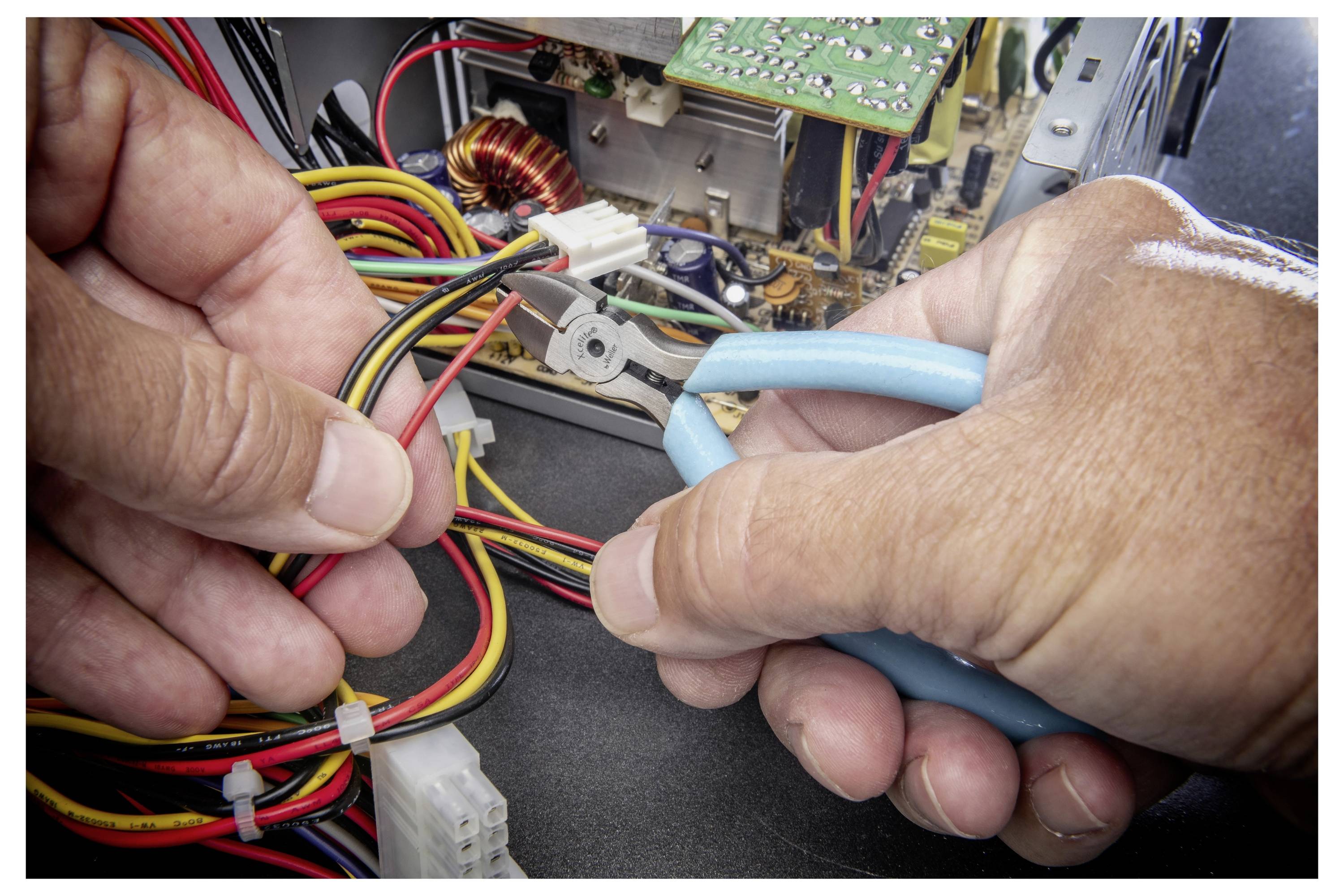 Hände verwenden blaue Zange zum Trennen von Verdrahtung in einem Computer oder elektronischen Gerät, mit freiliegenden Kabeln und Leiterplatten.