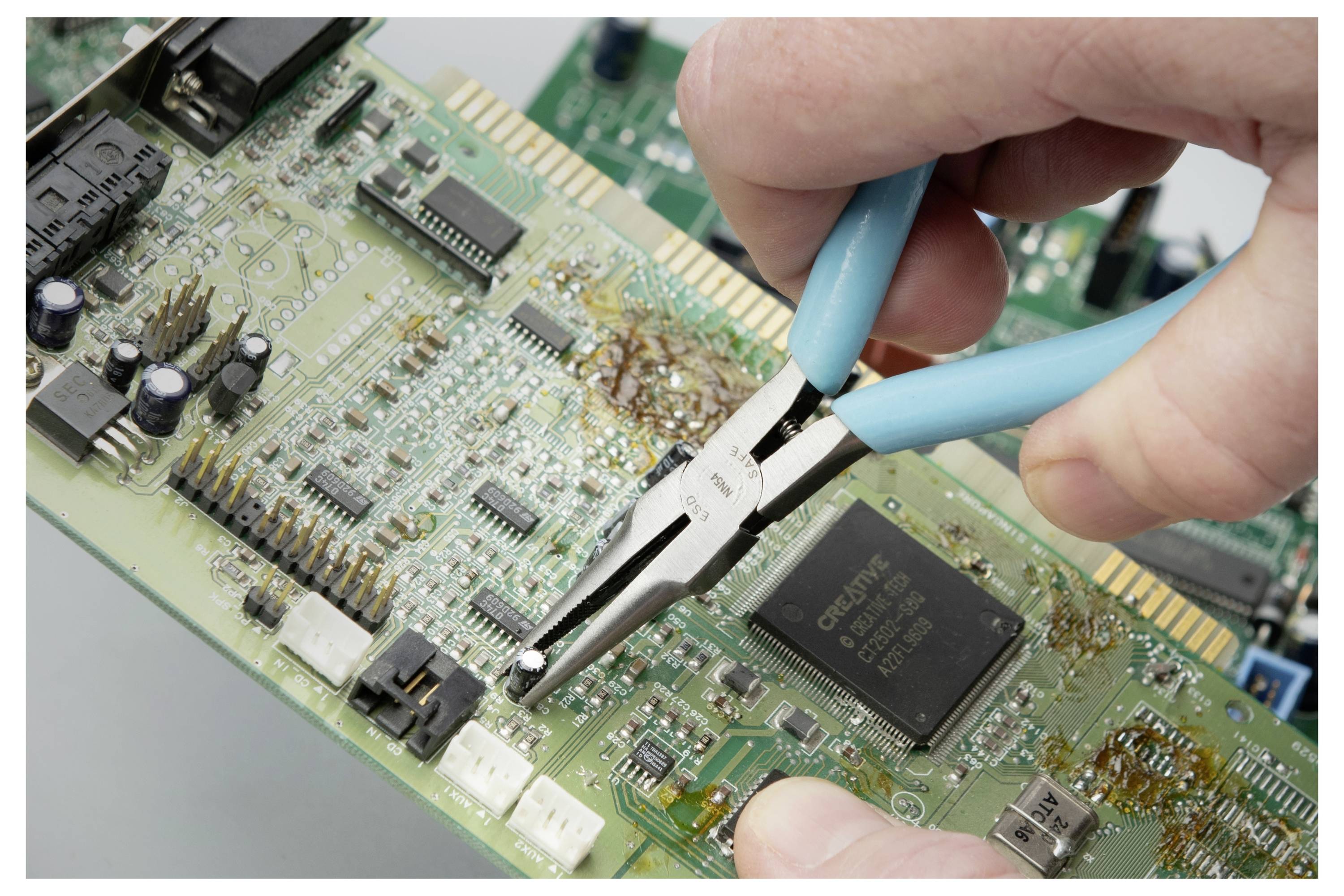 Nahaufnahme einer Hand, die mit einer Zange eine Komponente von einer Leiterplatte entfernt, zeigt elektronische Reparatur oder Demontage.