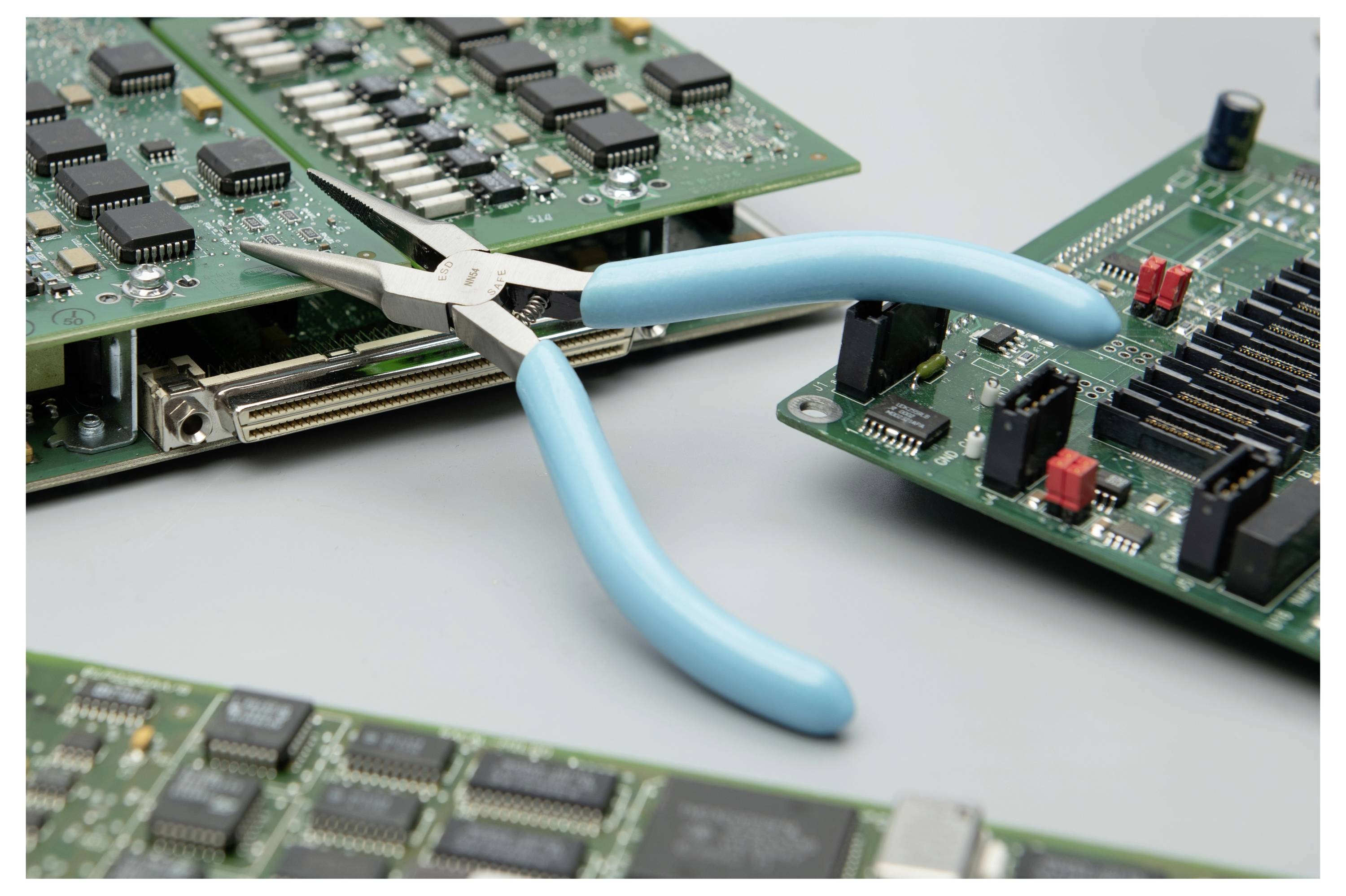 Blau griffe Zange hält eine elektronische Leiterplatte, was auf die Reparatur oder Demontage von Computerhardware hindeutet.