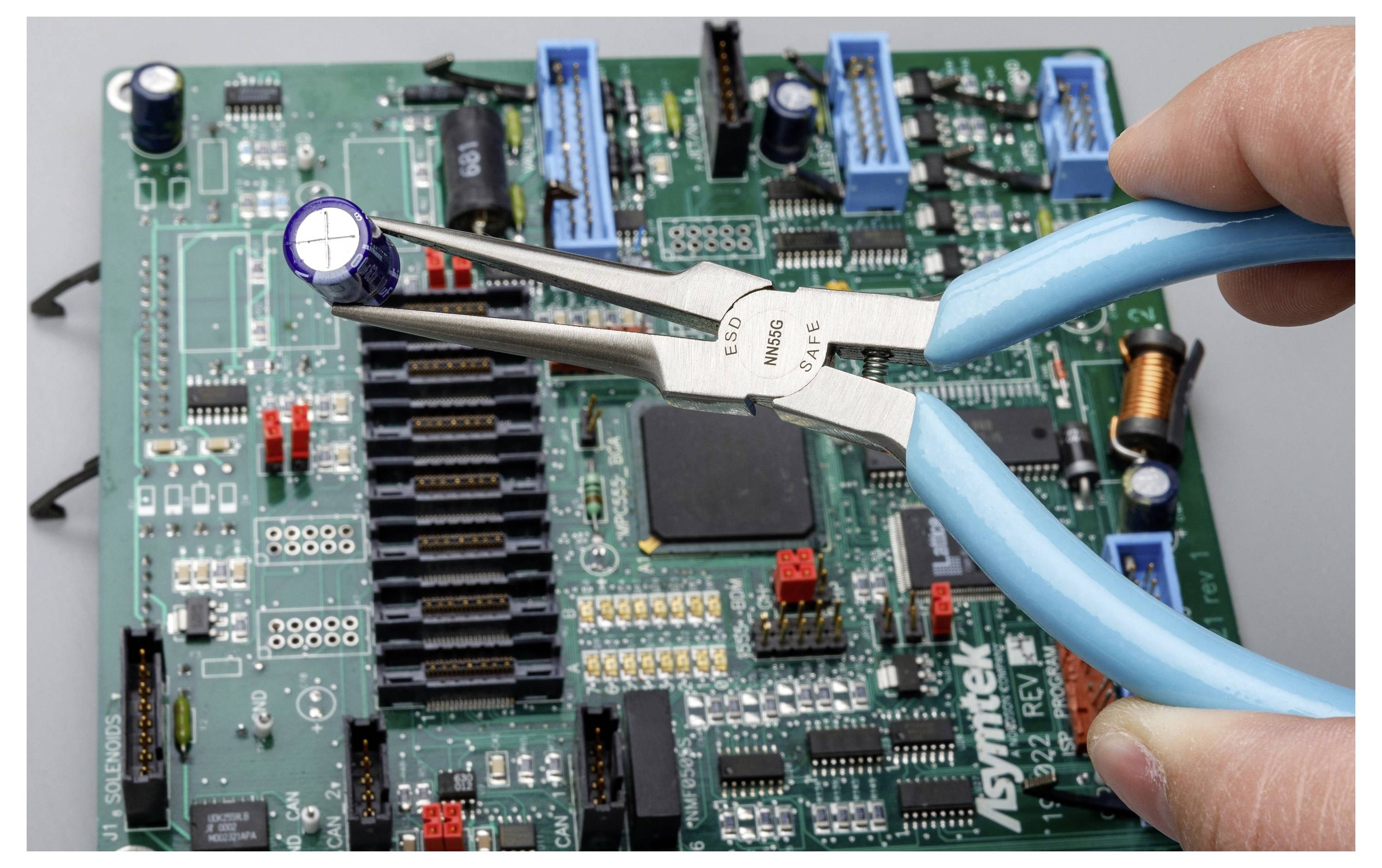 Eine Hand hält eine blaue Zange und entfernt einen Kondensator von einer Leiterplatte, was auf eine elektronische Reparatur oder Komponentenentfernung hindeutet.