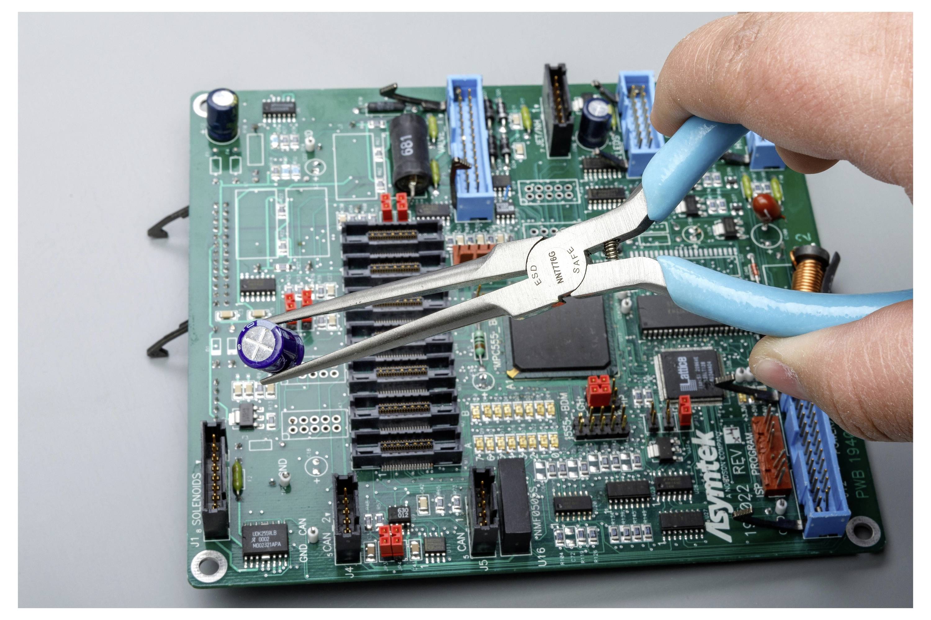 Eine Hand verwendet Pinzetten mit blauem Griff, um ein Bauteil auf einer grünen Leiterplatte oder elektronischen Hauptplatine einzustellen.