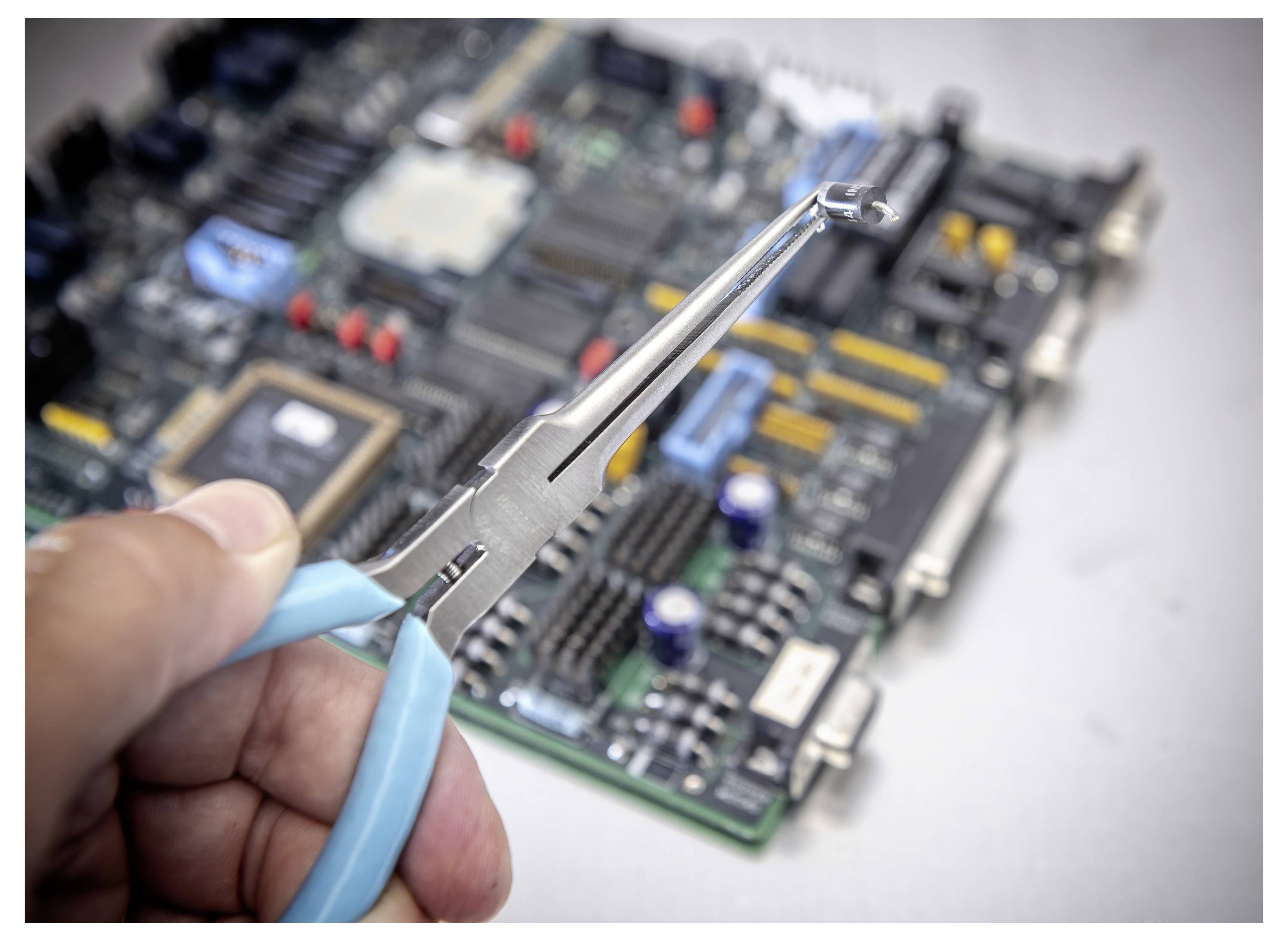 Eine Hand hält eine Spitzenzange über einer Computermainboard, was auf eine Elektronikreparatur oder Bauteilentfernung hindeutet.