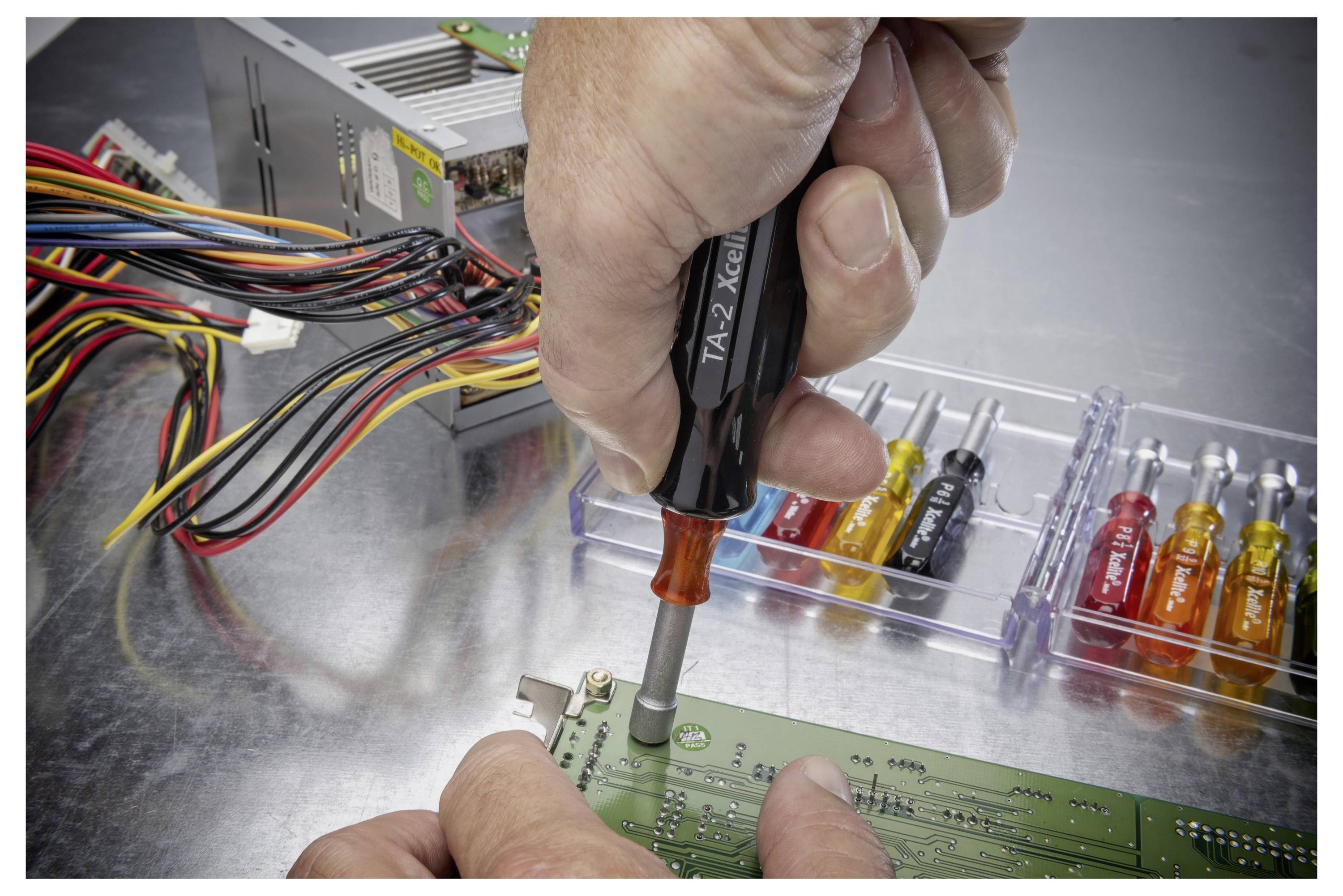 Handstraffen einer Schraube auf einer Leiterplatte in einem Computernetzteil, mit farbigen Drähten und kleinen Schraubenziehern in der Nähe.