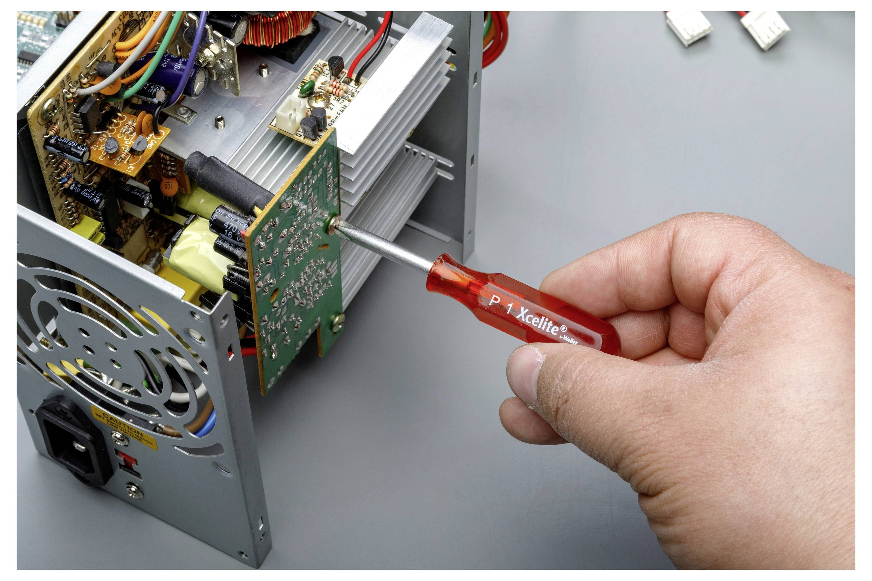 Hand mit einem Schraubendreher, um ein offenes elektronisches Gerät mit freiliegenden Leiterplatten und Verkabelung zu justieren.