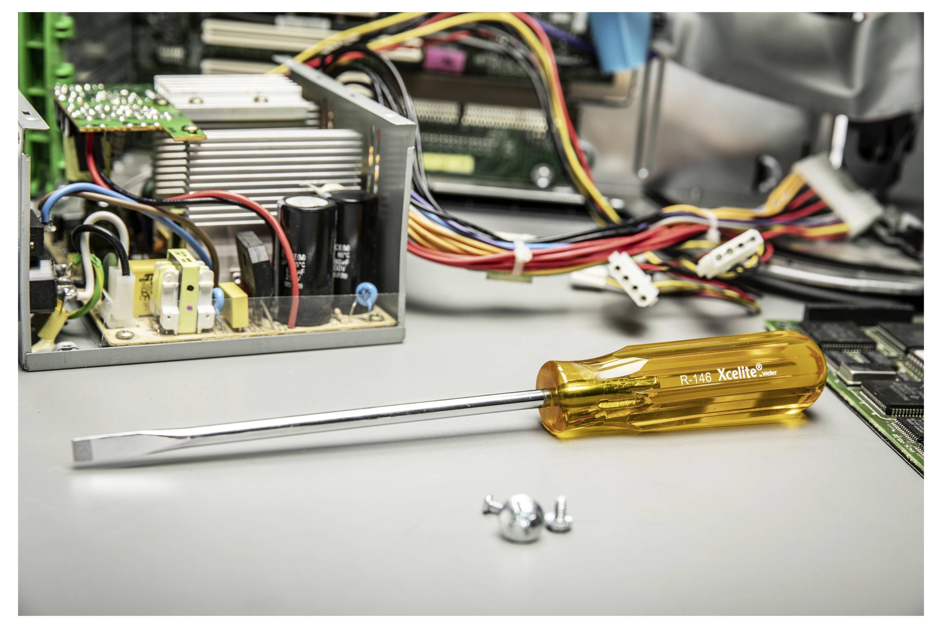 Schraubendreher mit gelbem Griff liegt auf einer Werkbank neben Computerhardware und losen Schrauben und deutet auf PC-Reparatur oder -Zusammenbau hin.