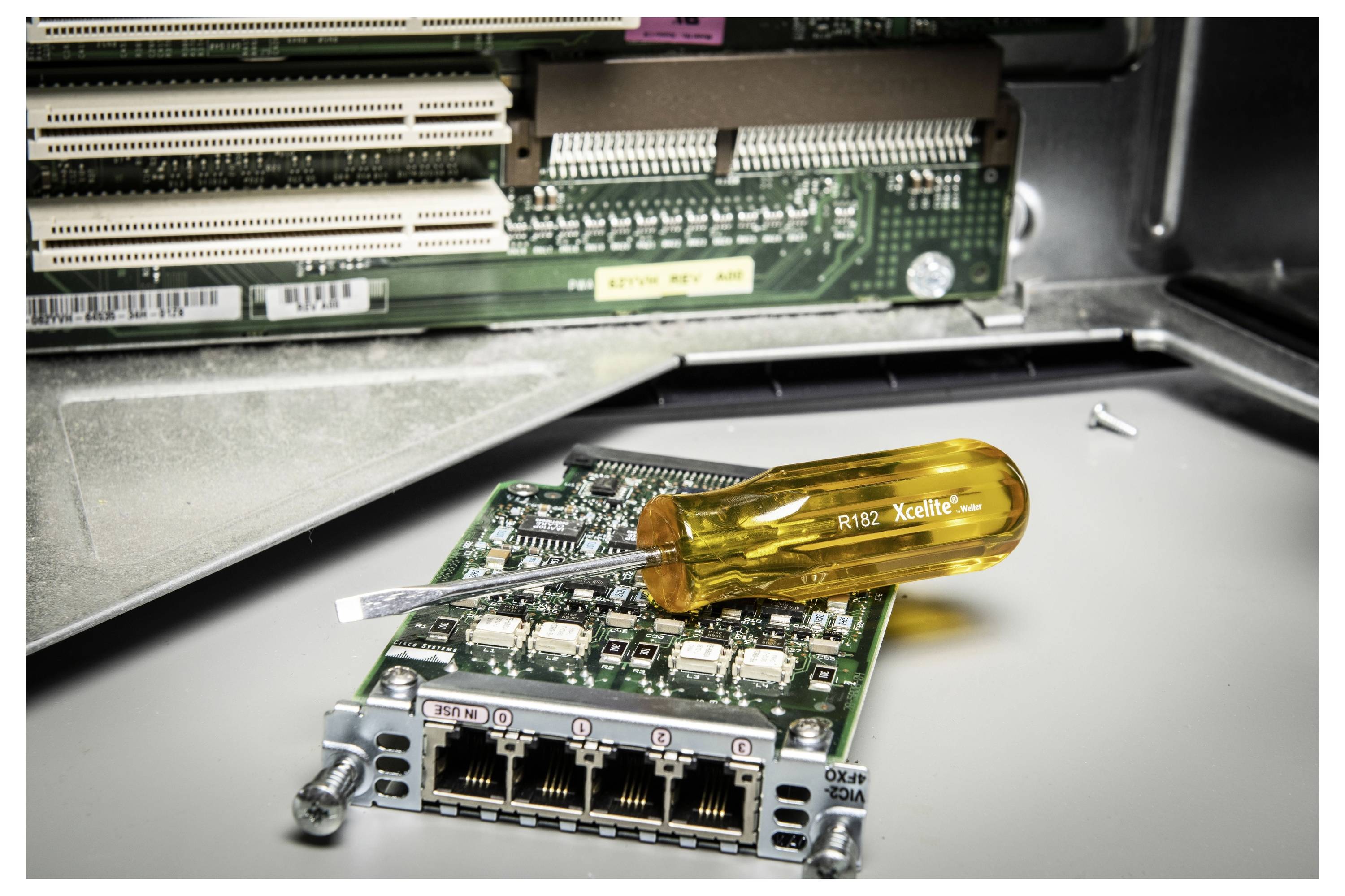 Ein Netzwerk-Switch-Modul liegt auf einer Metallfläche mit einem Schraubendreher mit gelbem Griff, der darauf ruht, innerhalb eines offenen Server- oder Netzwerk-Racks.