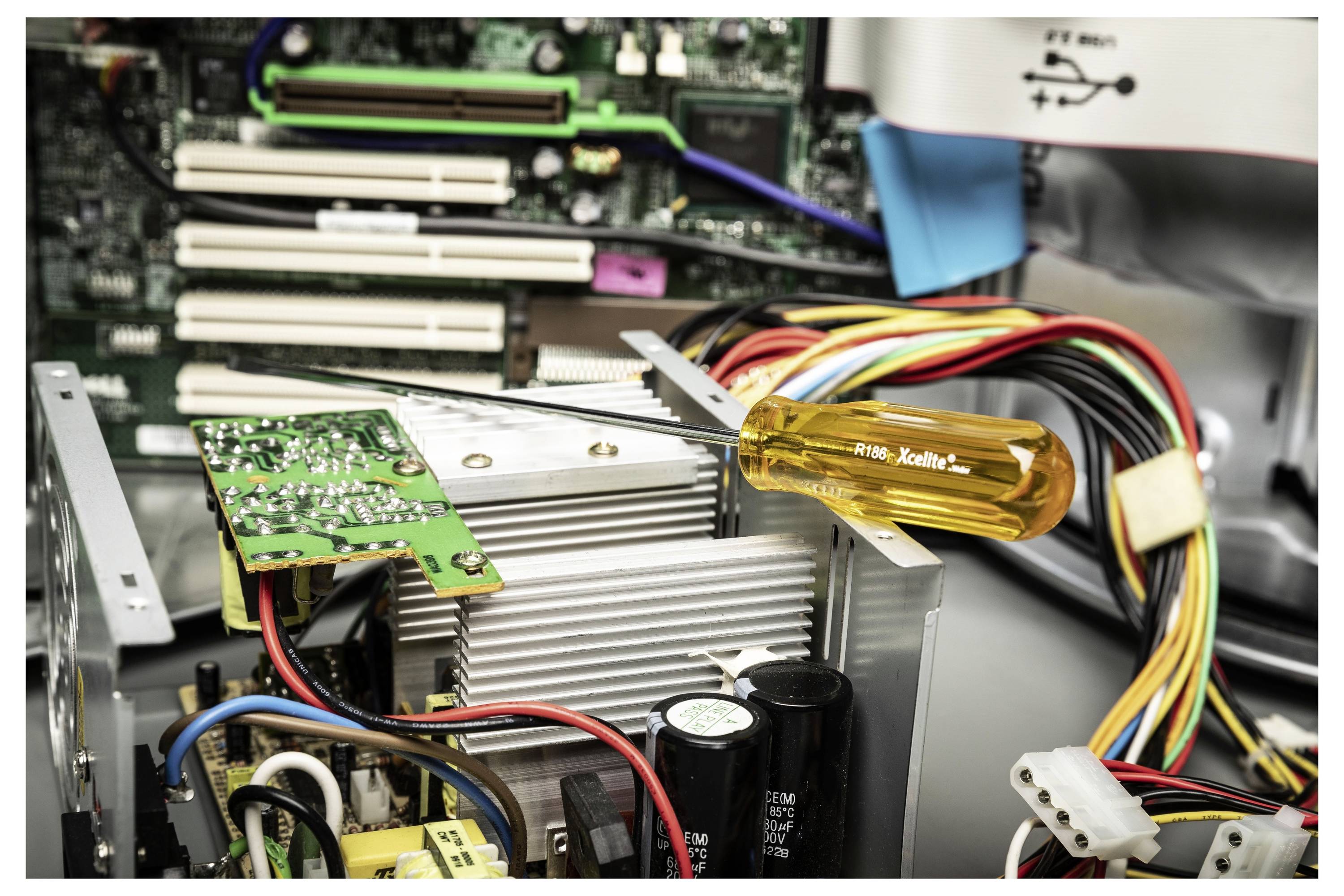 Nahaufnahme eines offenen Computergehäuses mit sichtbarer Innenhardware: Motherboard, Kühlkörper, Kabel, Stromstecker und ein Schraubenzieher, der auf den Komponenten ruht.