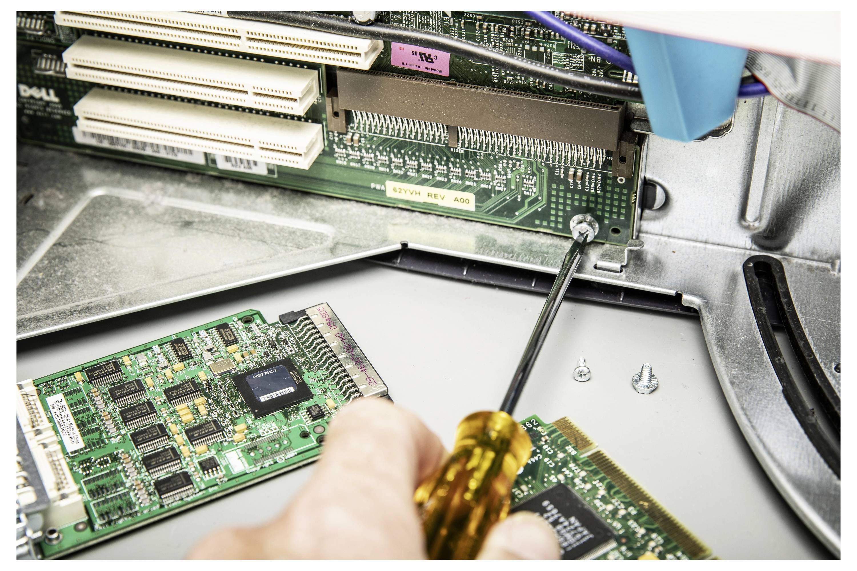 Eine Hand schraubt eine Computerplatine in einem offenen Desktop-Gehäuse ab, wobei interne Kabel und Erweiterungskarten sichtbar sind.