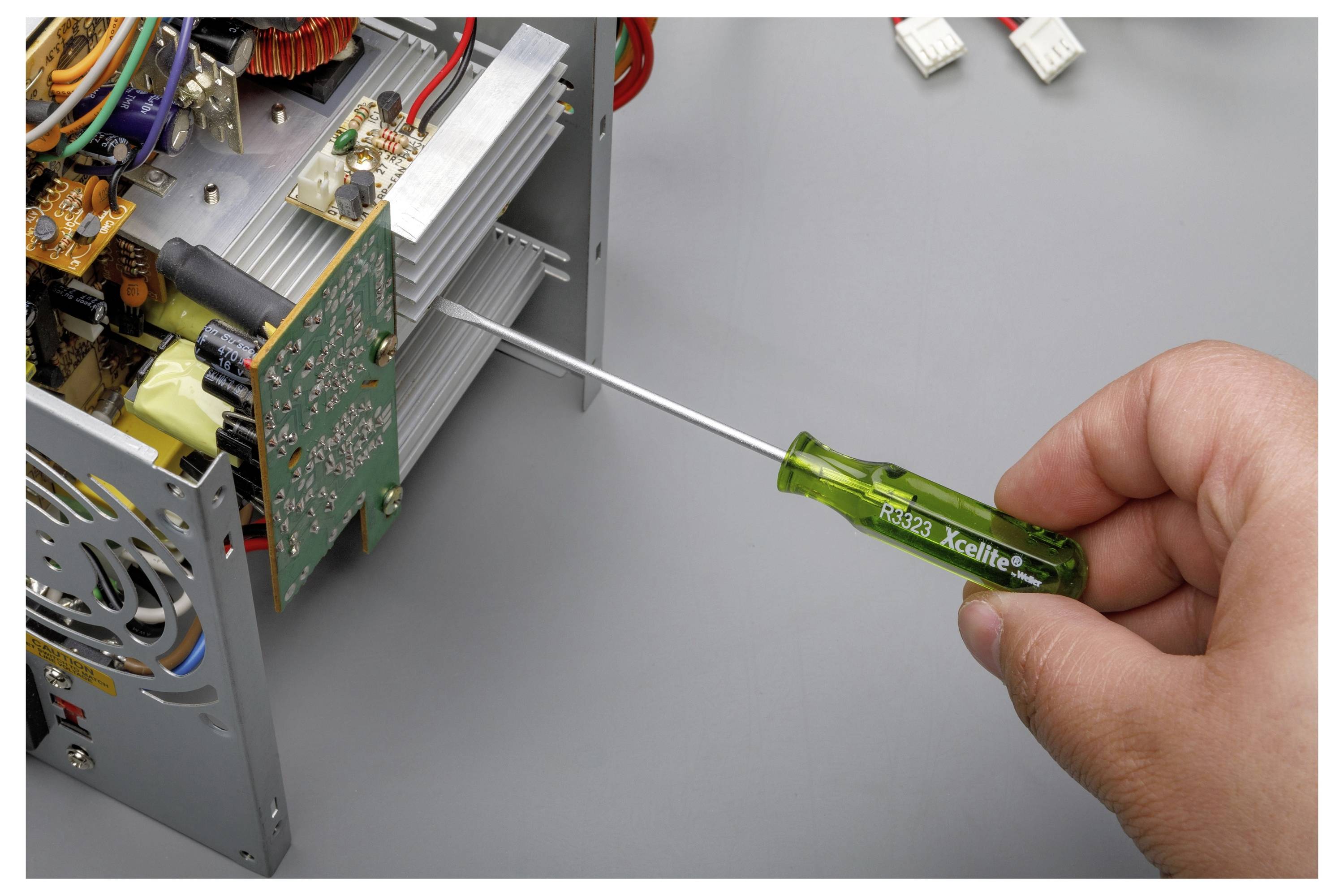 Hand mit einem grünen Schraubendreher zur Anpassung eines elektronischen Schaltkreises in einem offenen Metallgerätechassis.