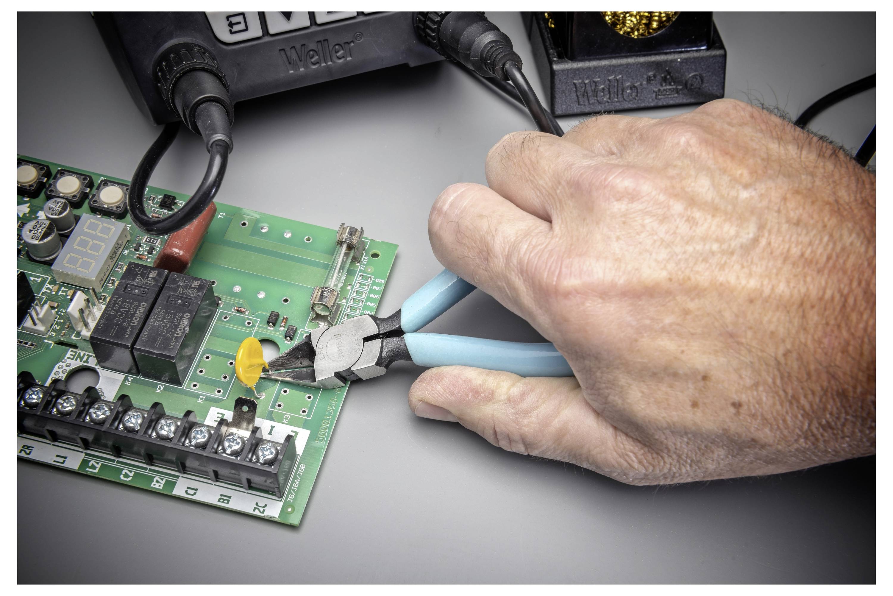 Hand mit Zange zum Anpassen oder Schneiden eines Drahts auf einer elektronischen Leiterplatte während der Reparaturarbeit.