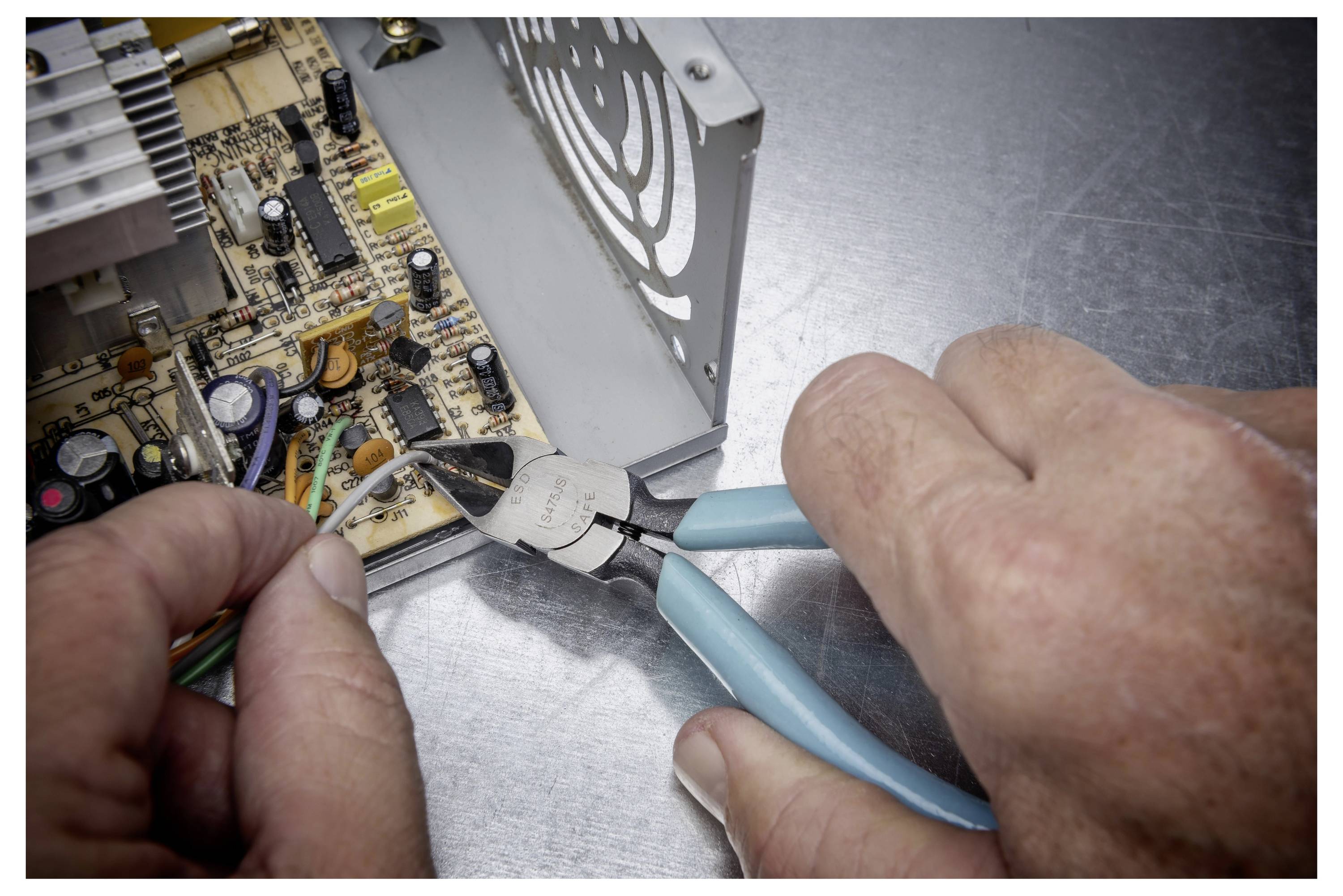 Hände verwenden Zangen zum Schneiden von Drähten während der Reparatur einer Leiterplatte in einem Elektronikgerät.