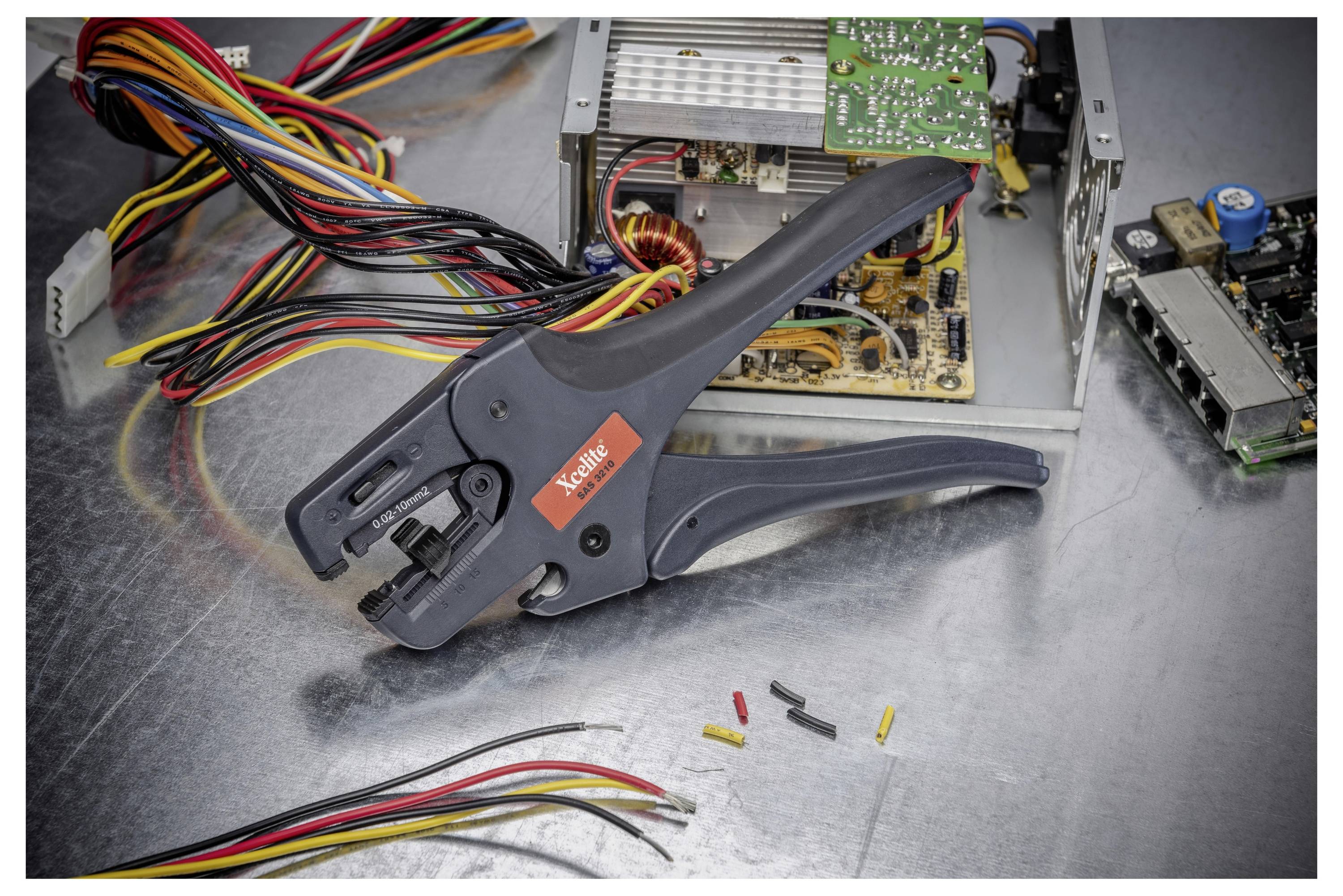 Quetschzange für Drähte auf einer Metallwerkbank mit mehrfarbigen Kabeln, losen Steckverbindern und einem offenen elektronischen Gerät, das repariert wird.