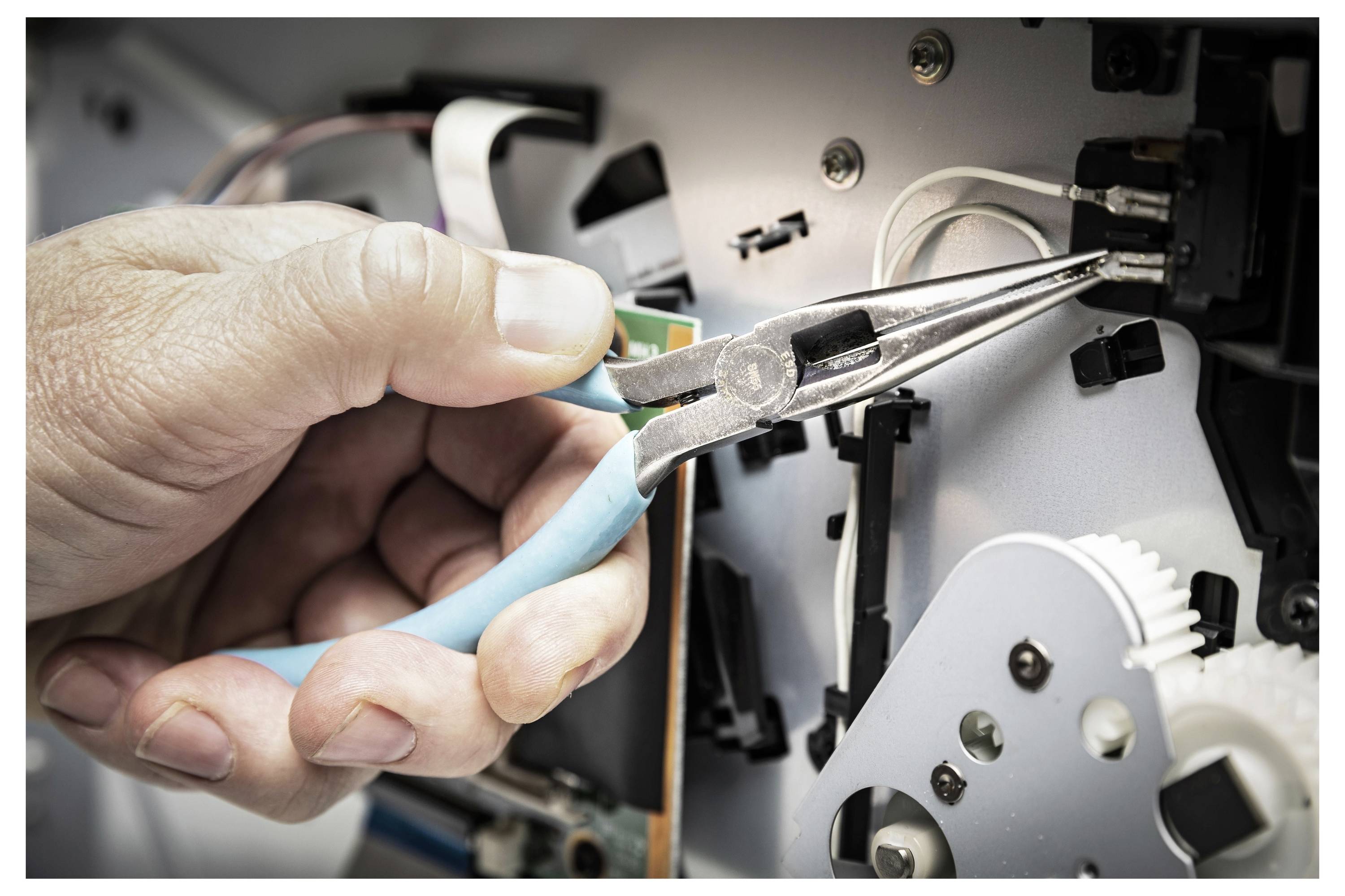 Nahaufnahme einer Hand, die eine Spitzenzange verwendet, um Drähte in einer Maschine oder einem elektrischen Gerät zu justieren.