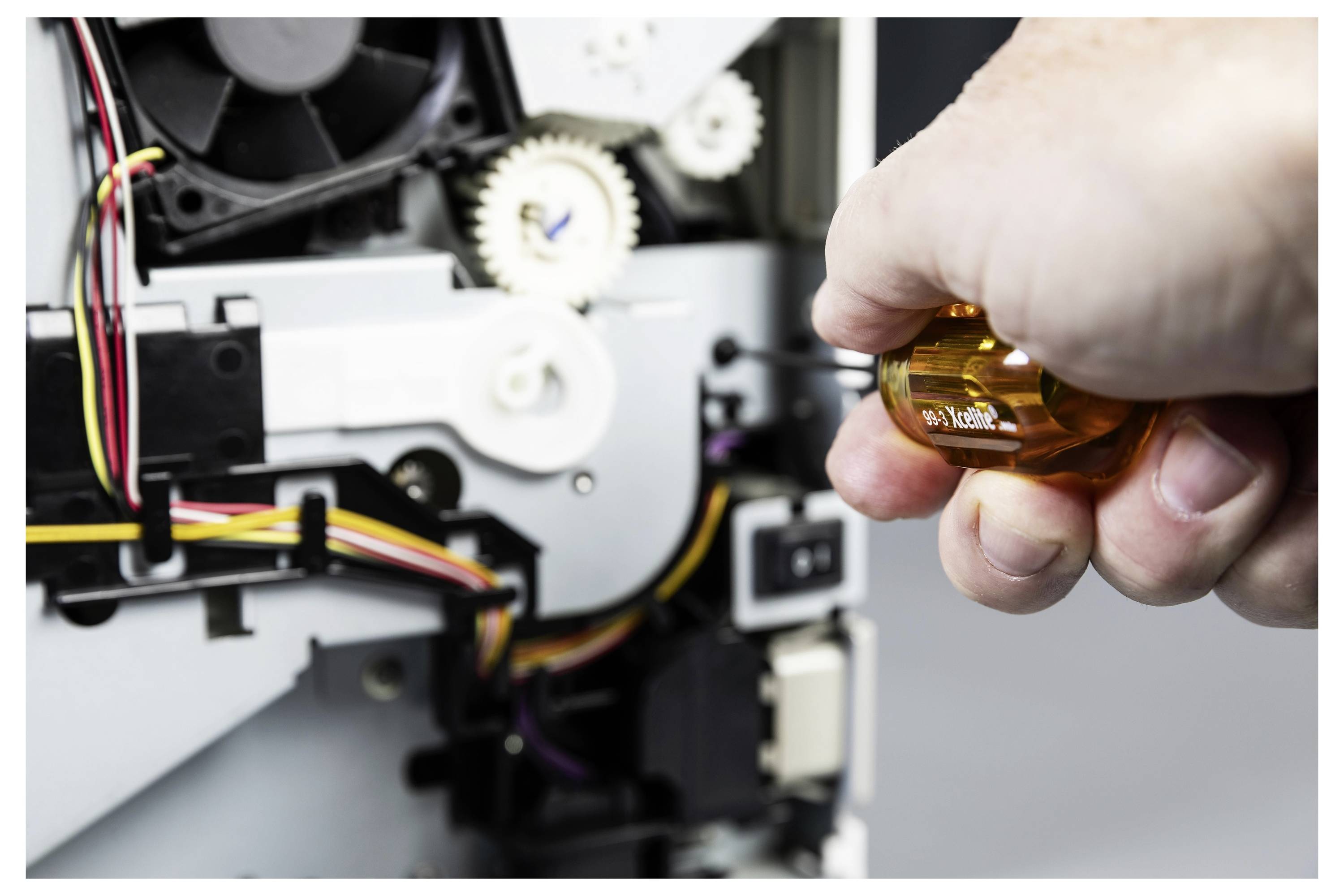 Eine Hand verwendet einen Schraubendreher, um die Zahnräder und Verdrahtung in einem elektronischen Gerät oder Drucker einzustellen.