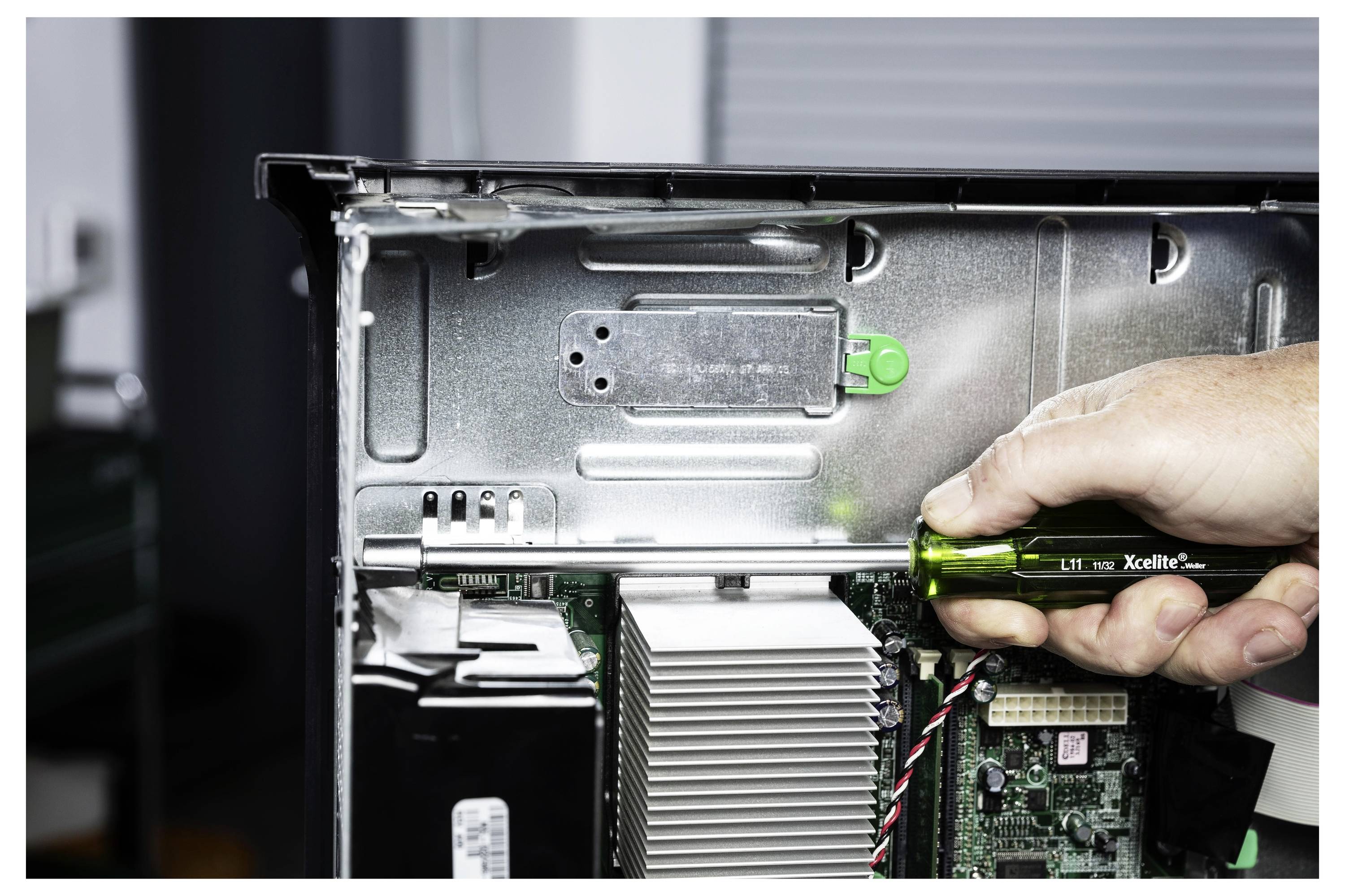 Eine Hand schraubt ein Computergheäusepanel mit einem grünen Schraubendreher ab und gibt damit das Motherboard und den Kühlkörper im Desktop-Tower frei.
