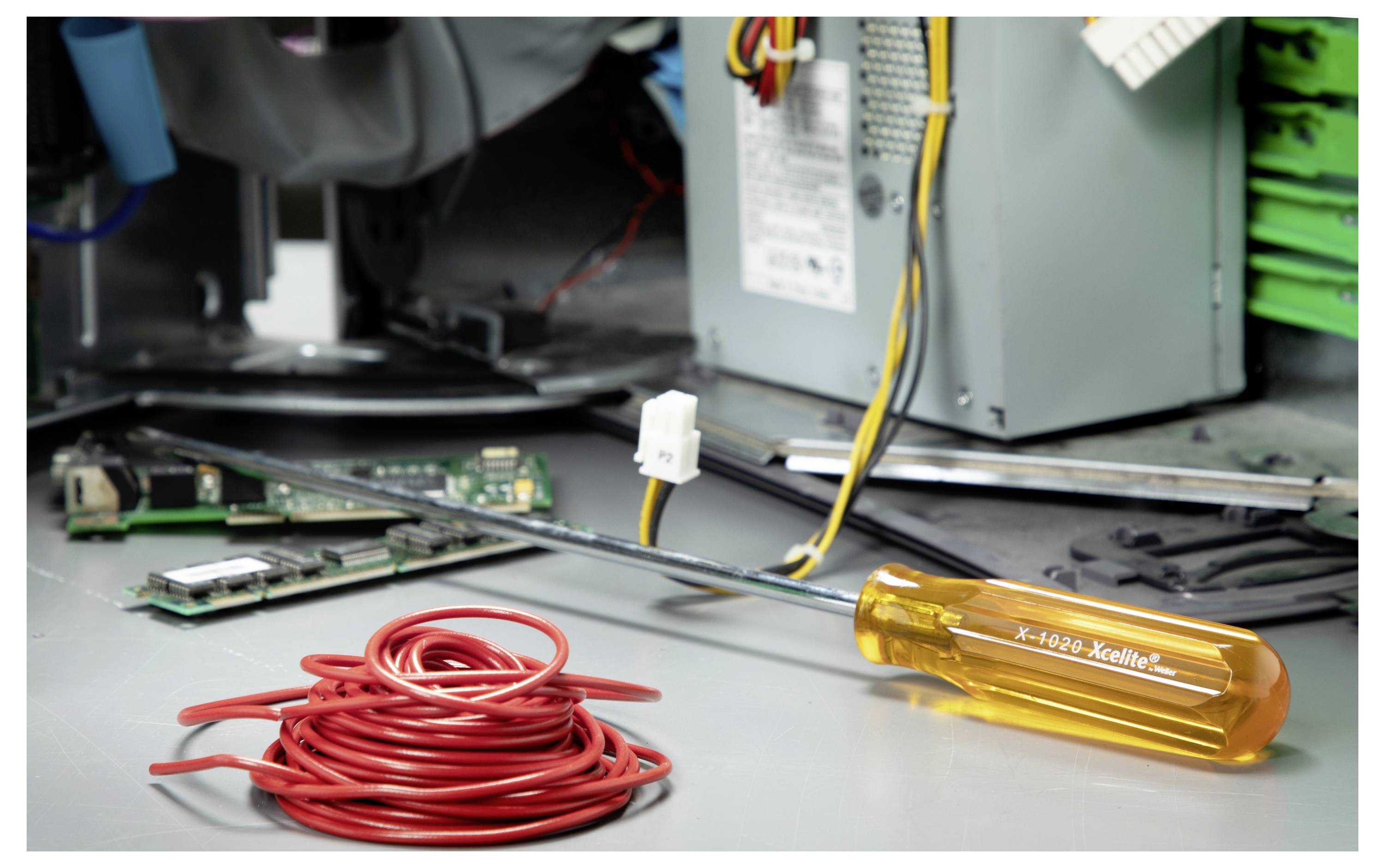 Offenes Computergehäuse mit roter Kabelspule und orangefarbenem Schraubendreher auf dem Metallrahmen, was auf PC-Reparatur oder Montage hindeutet.