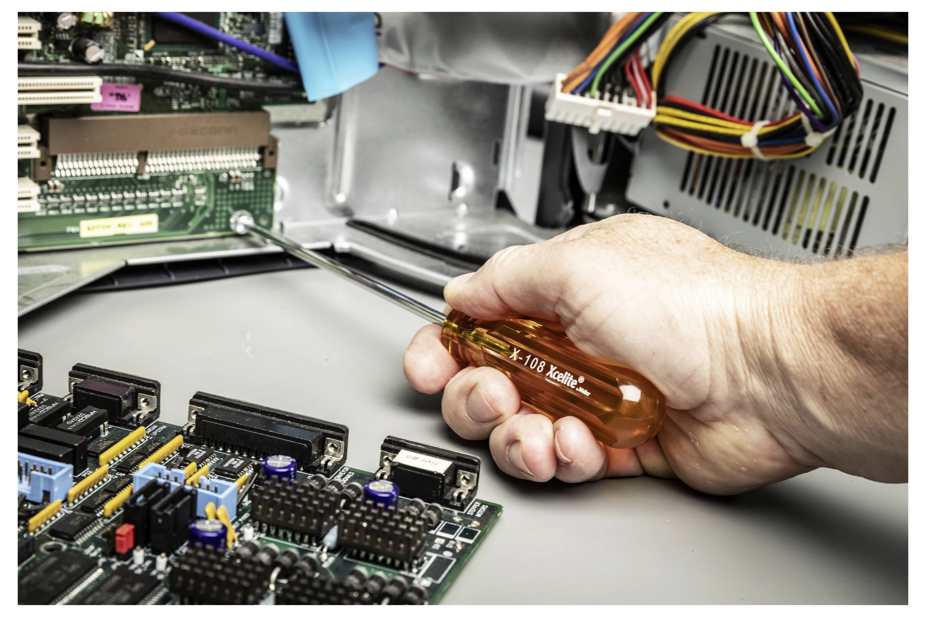Eine Hand, die einen Schraubendreher verwendet, um in einem offenen Computer oder elektronischen Gerät zu arbeiten, mit sichtbaren Leiterplatten und gebündelten Kabeln.