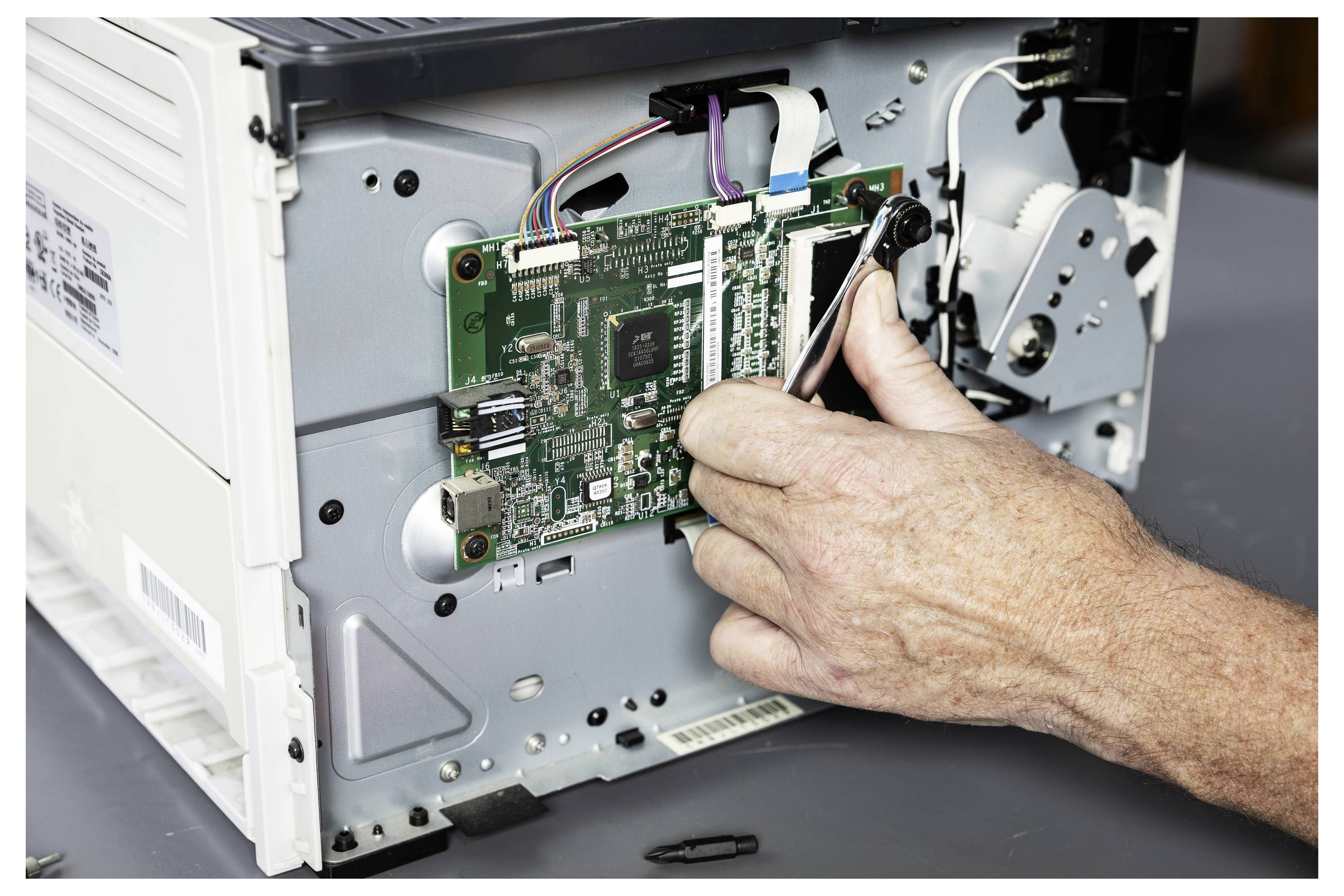 Hände installieren eine Leiterplatte in einem offenen elektronischen Gerät mit angeschlossenen Kabeln und freiliegenden internen Komponenten.
