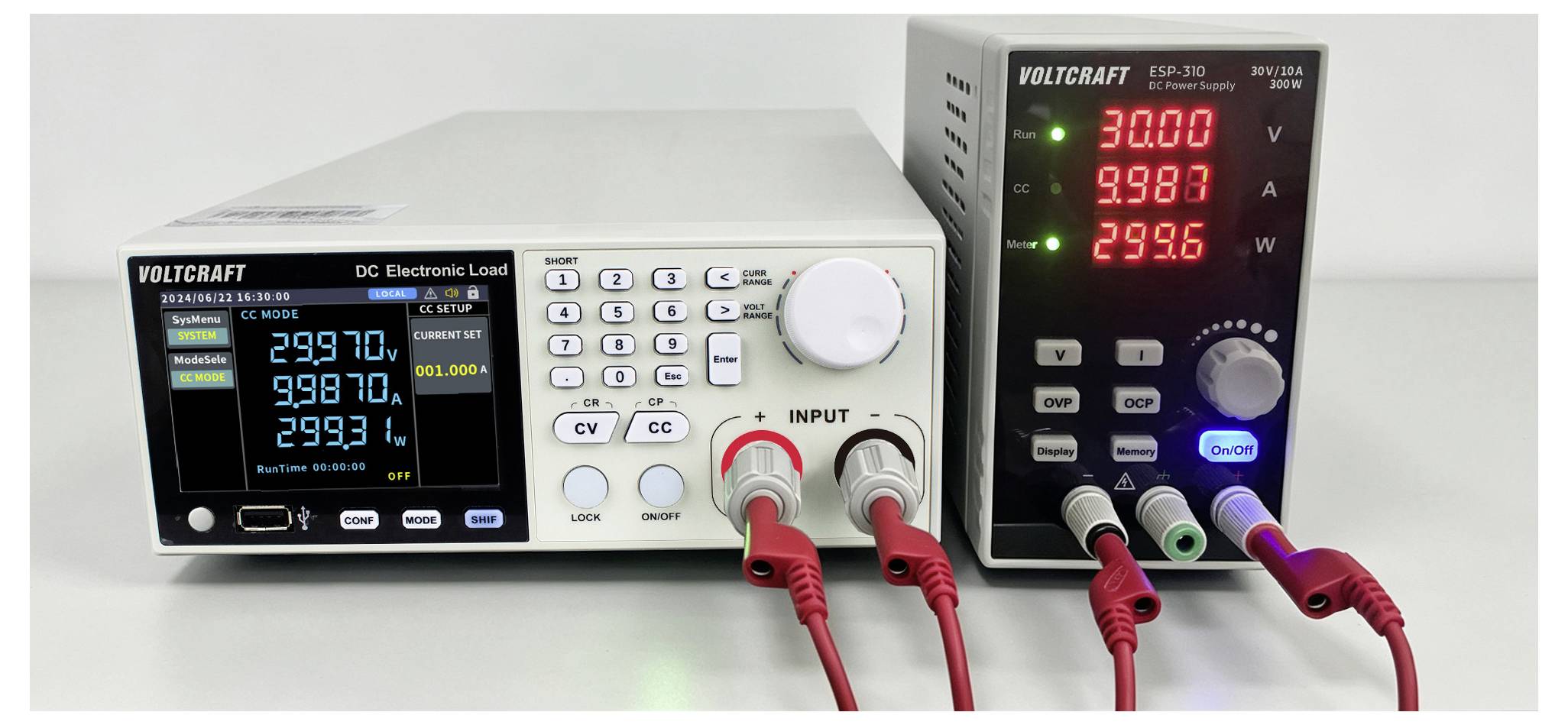 Zwei Voltcraft-Elektronik-Testinstrumente auf einer Werkbank, mit einer DC-Elektroniklast-Anzeige auf der linken Seite und einer Spannungs-/Strom-/Leistungsanzeige auf der rechten Seite, verbunden durch rote und schwarze Leitungen.