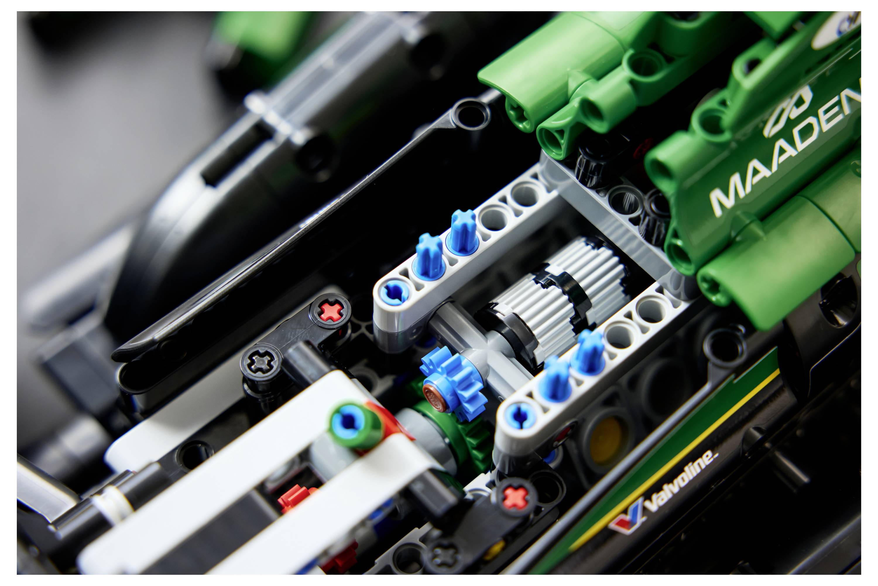 Nahaufnahme eines LEGO Technic Fahrzeugmotors mit sichtbaren blauen Zahnrädern und grünem 