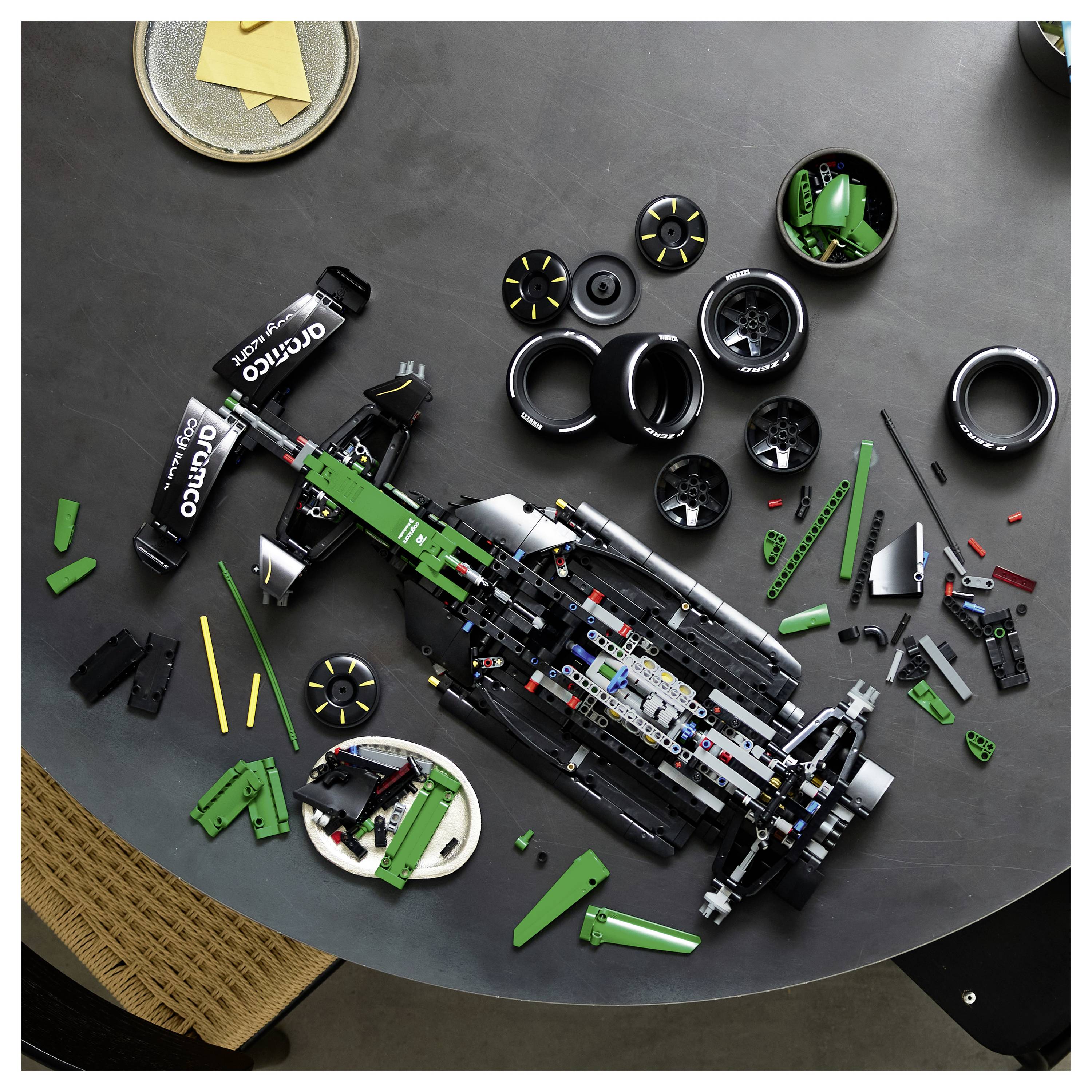 Draufsicht eines teilweise zusammengesetzten LEGO Formel-1-Rennwagens mit verstreuten Rädern und Teilen auf einem Tisch.