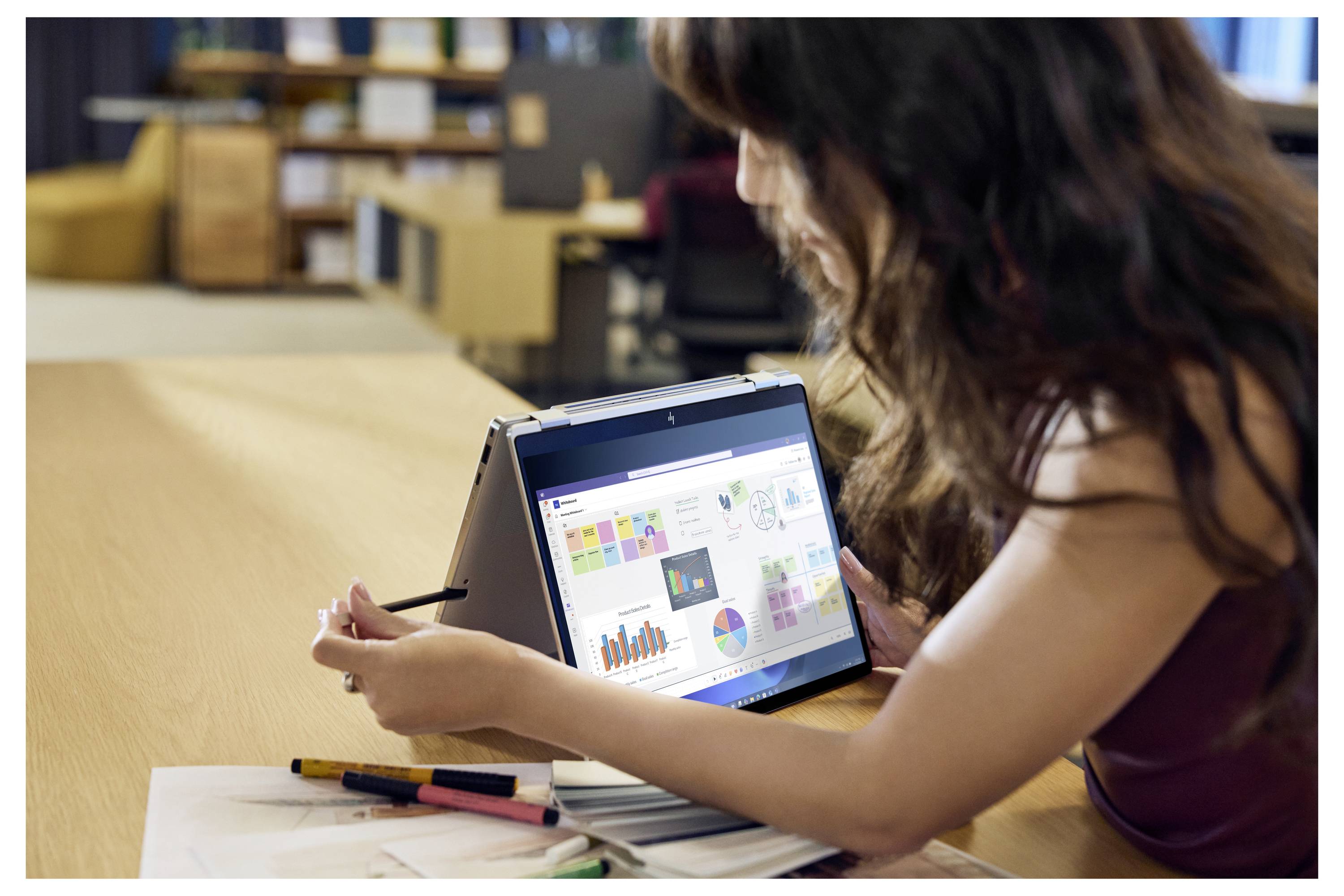 Frau, die ein Tablet auf einem Ständer nutzt, um bunte Diagramme und Grafiken an einem Schreibtisch zu überprüfen, mit einem Stift und Notizbuch in der Nähe.